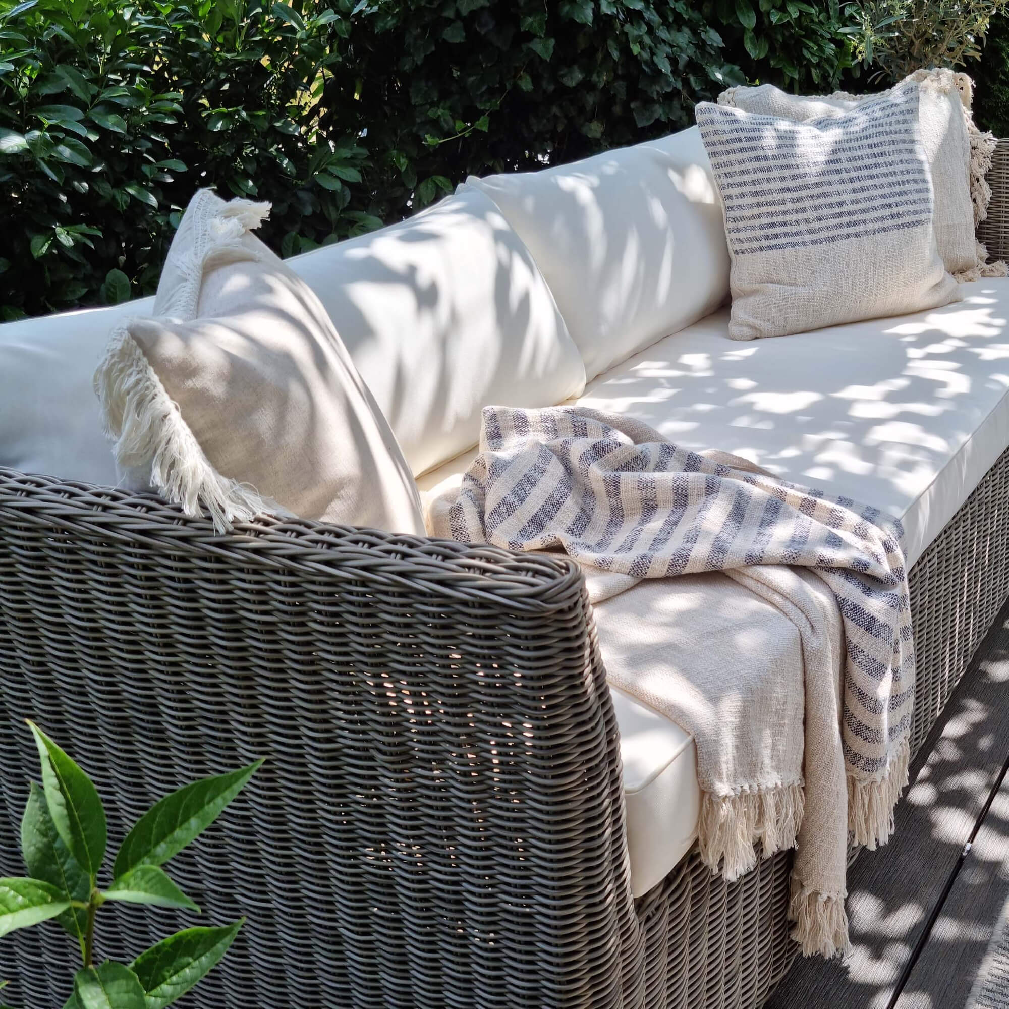 Divano da giardino in rattan grigio con cuscini crema e coperta beige a righe