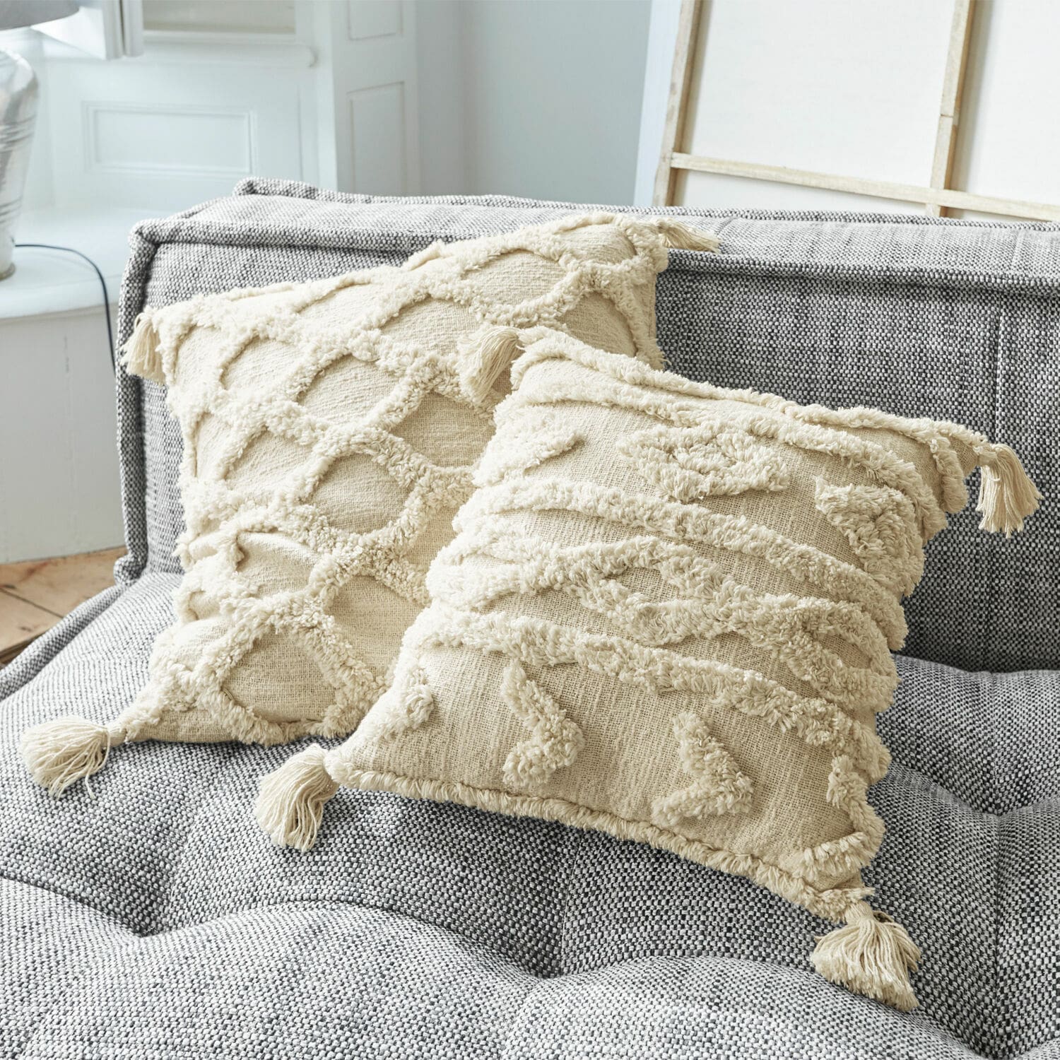 Coppia di copricuscini Linares Cuscini decorativi in cotone beige con frange e motivi testurizzati su divano grigio imbottito