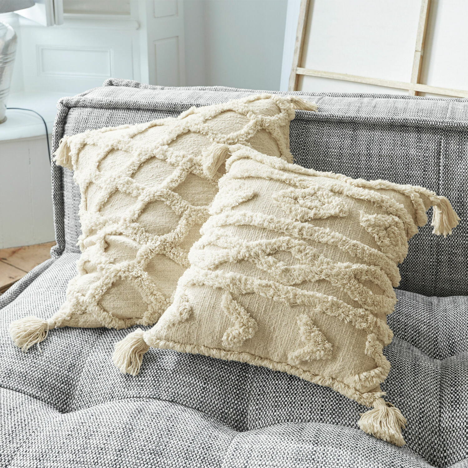Coppia di copricuscini Linares Cuscini decorativi in cotone beige con frange e motivi testurizzati su divano grigio imbottito