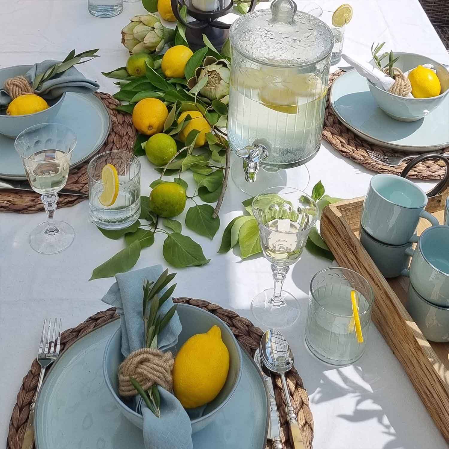 Tavola estiva con ceramica azzurra, limoni e foglie verdi su tovaglia bianca, decorazione tavola