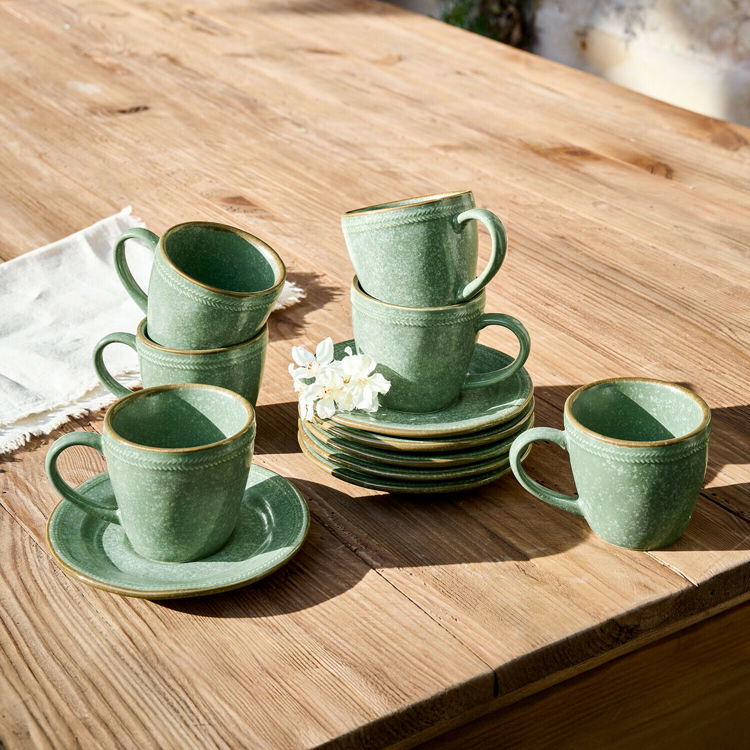 Set di tazze e piattini in ceramica verde su tavolo in legno con fiore decorativo