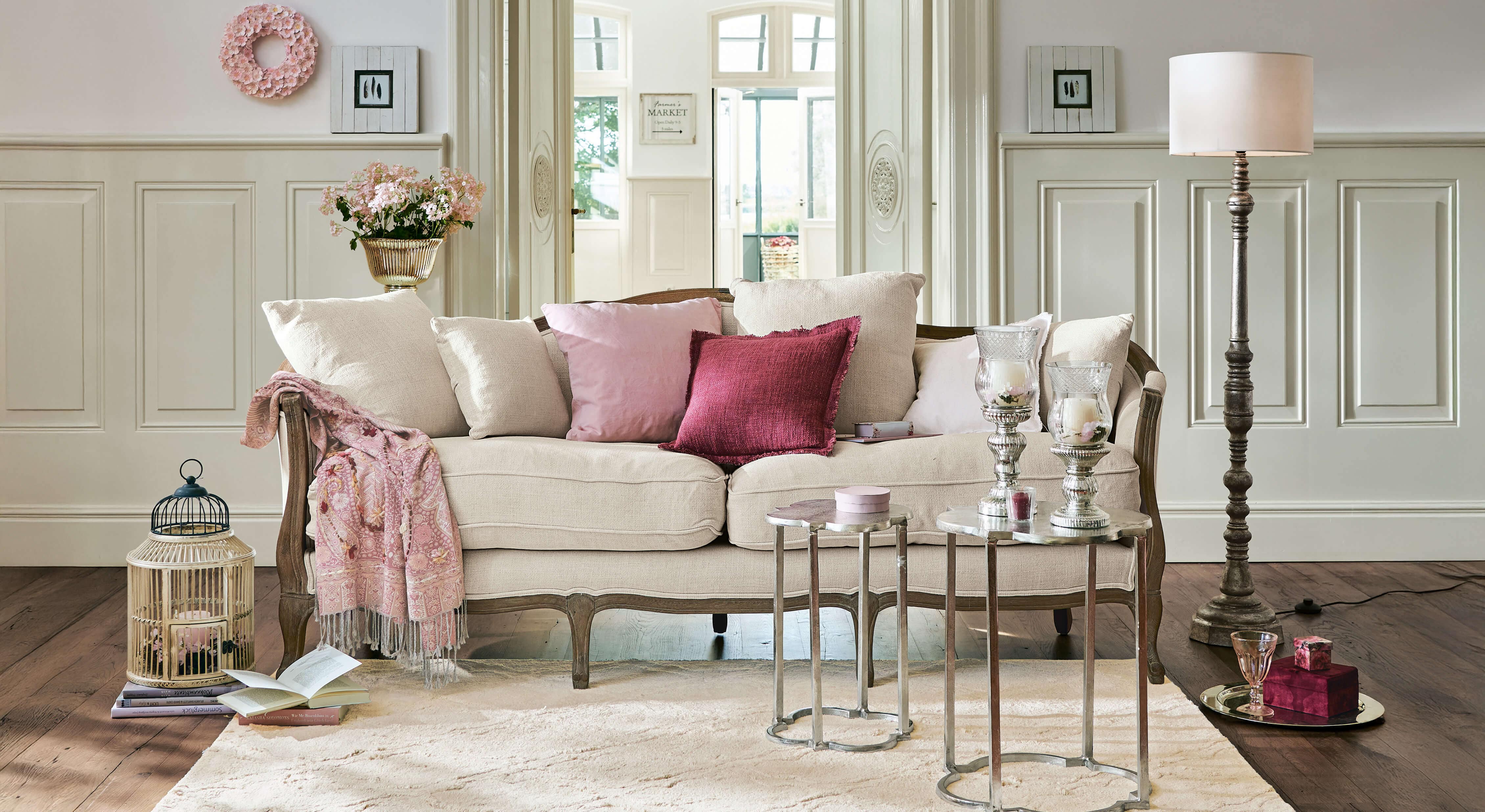 Divano beige con struttura in legno e cuscini rosa in soggiorno elegante con decorazioni