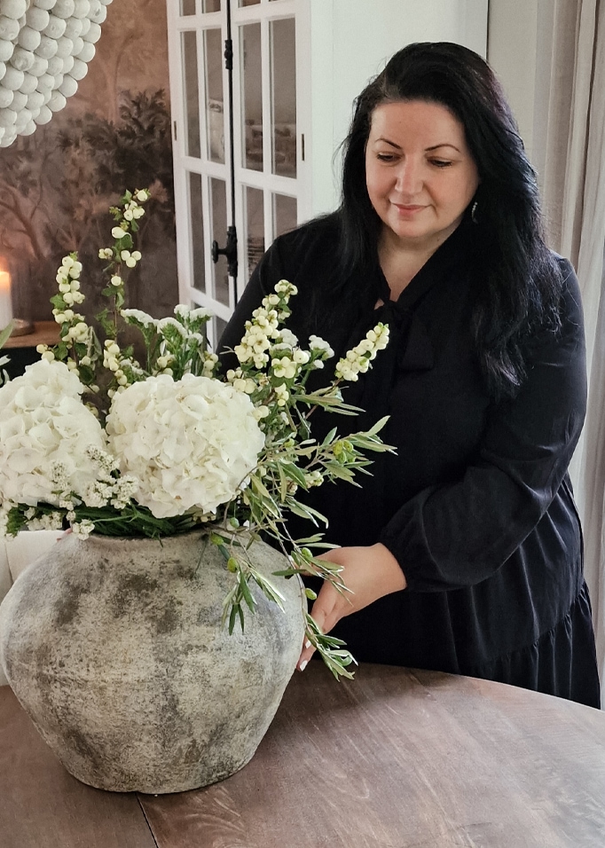 Grande vaso in pietra con fiori bianchi su tavolo in legno, donna con vestito nero sullo sfondo