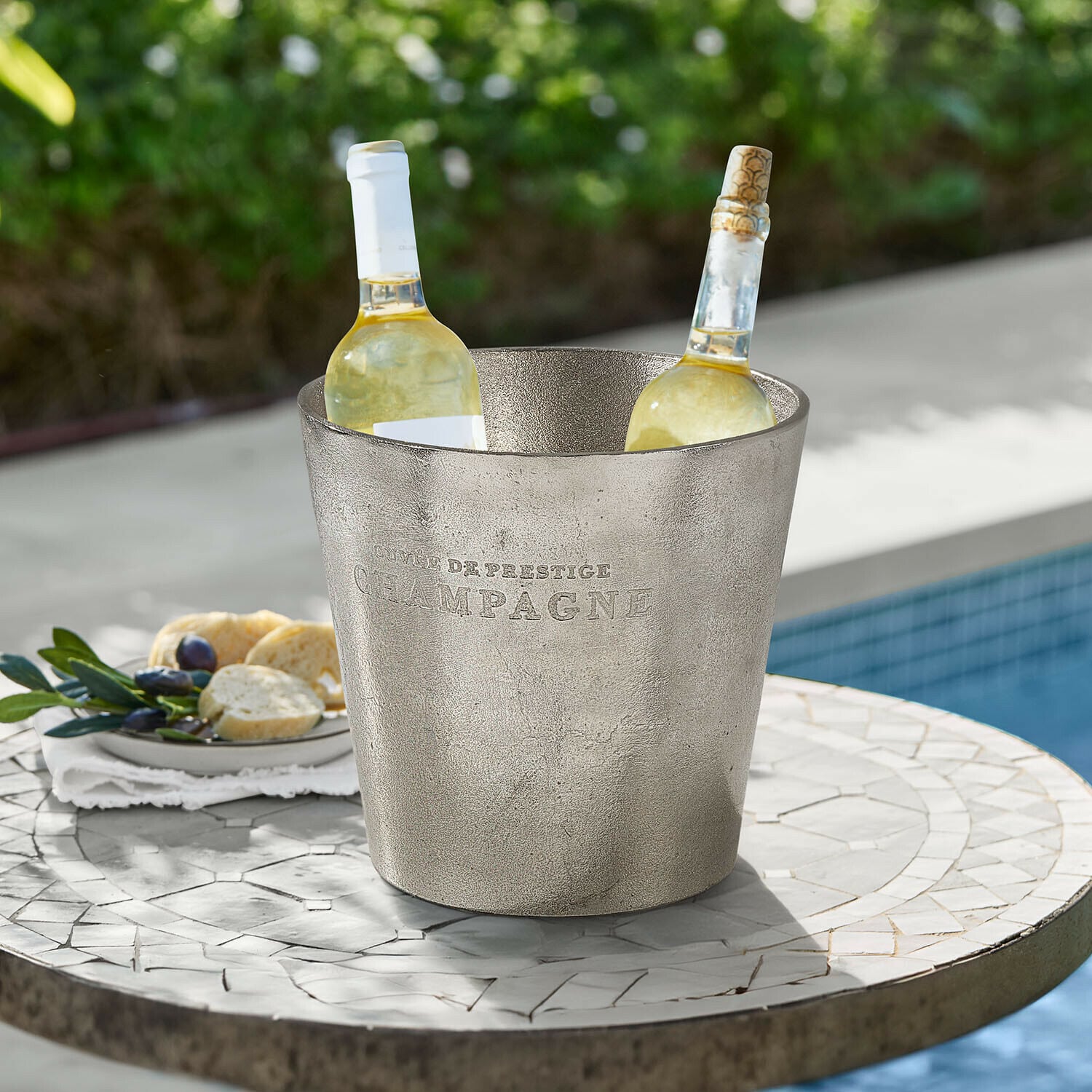 Secchiello del ghiaccio Marclaire Secchiello per ghiaccio in metallo argentato con scritta Champagne e due bottiglie di vino bianco su tavolo da giardino