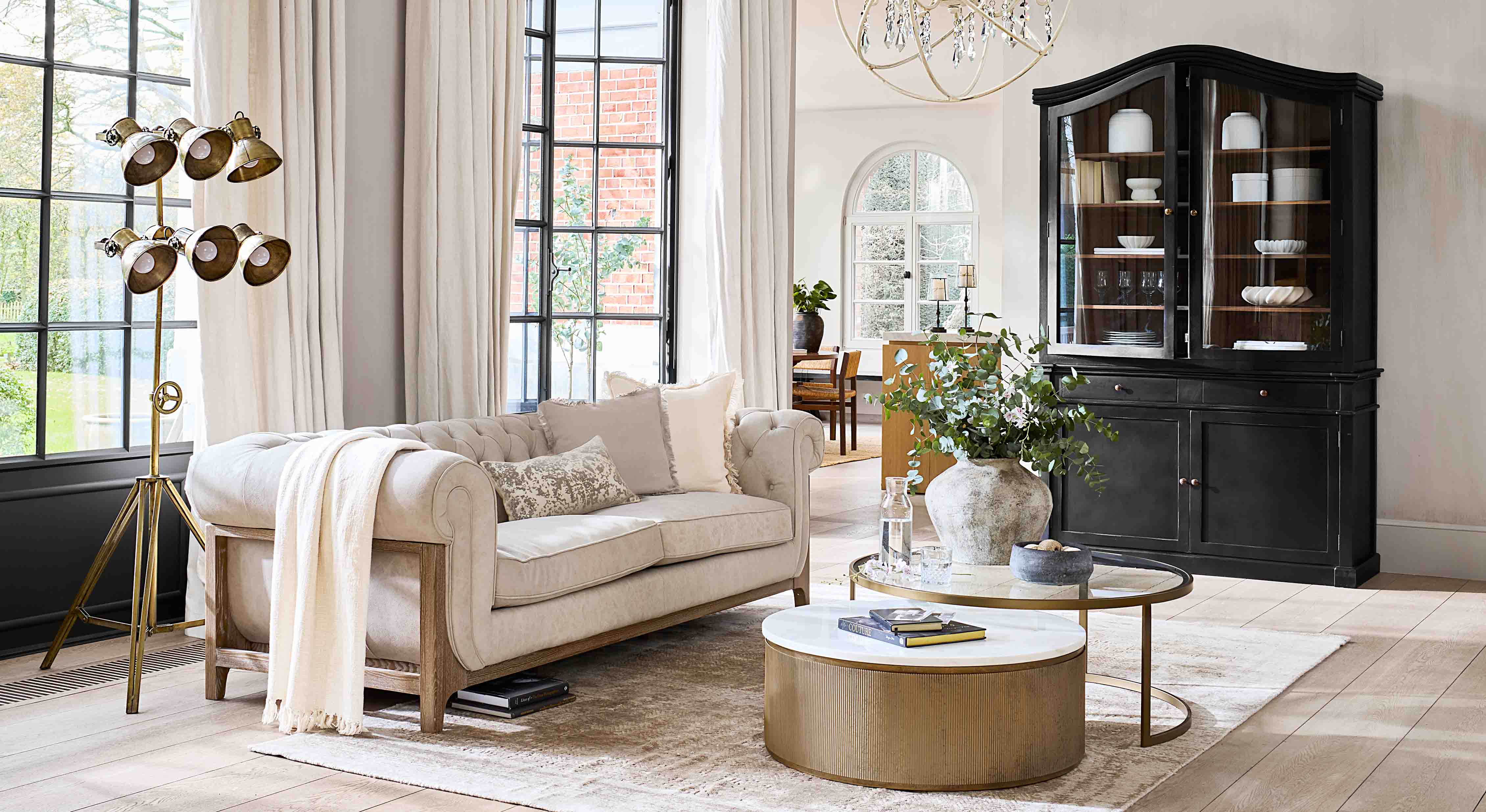 Divano beige con struttura in legno in soggiorno luminoso con vetrina nera e lampada da terra dorata
