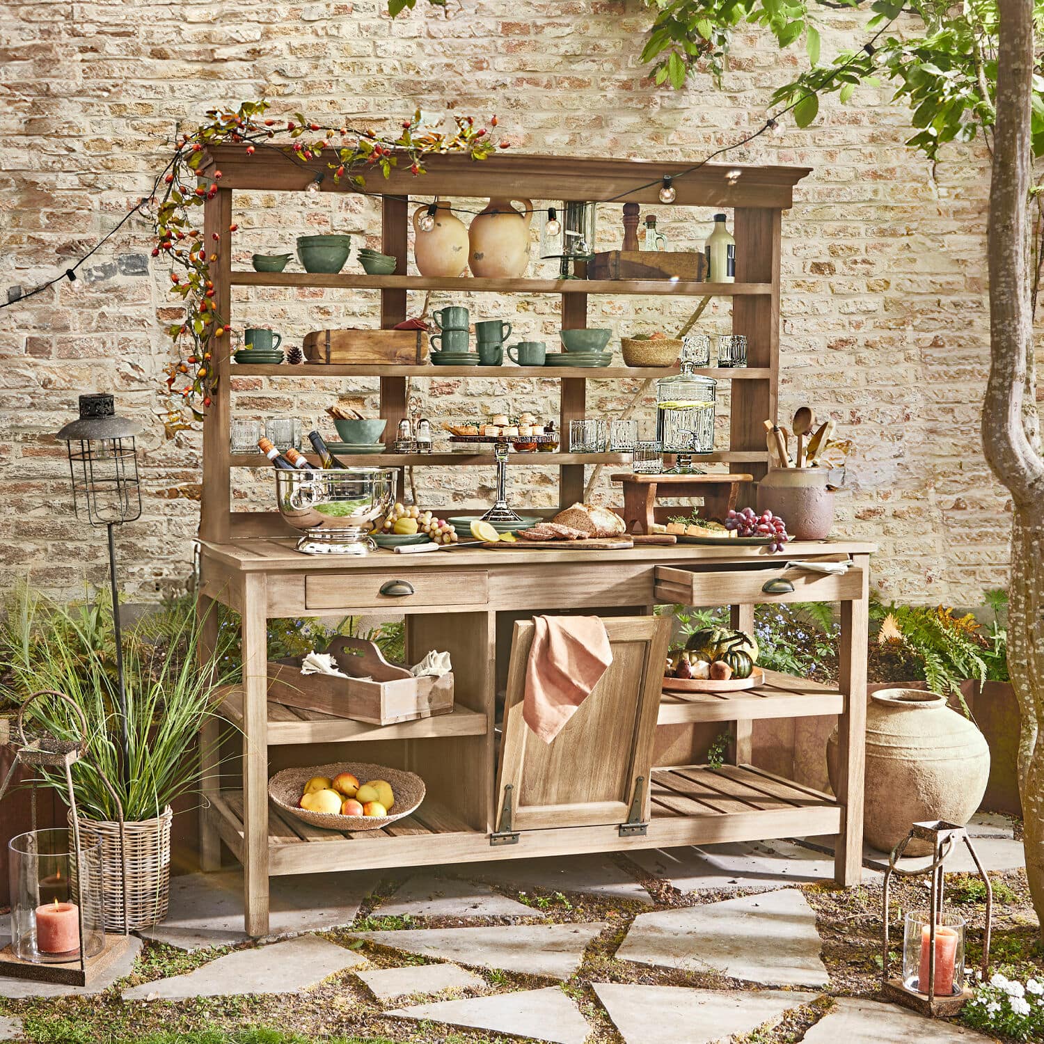 Mobile da giardinaggio Fallon Mobile da giardino in legno con scaffali e cassetti, decorato con stoviglie e cibo su patio