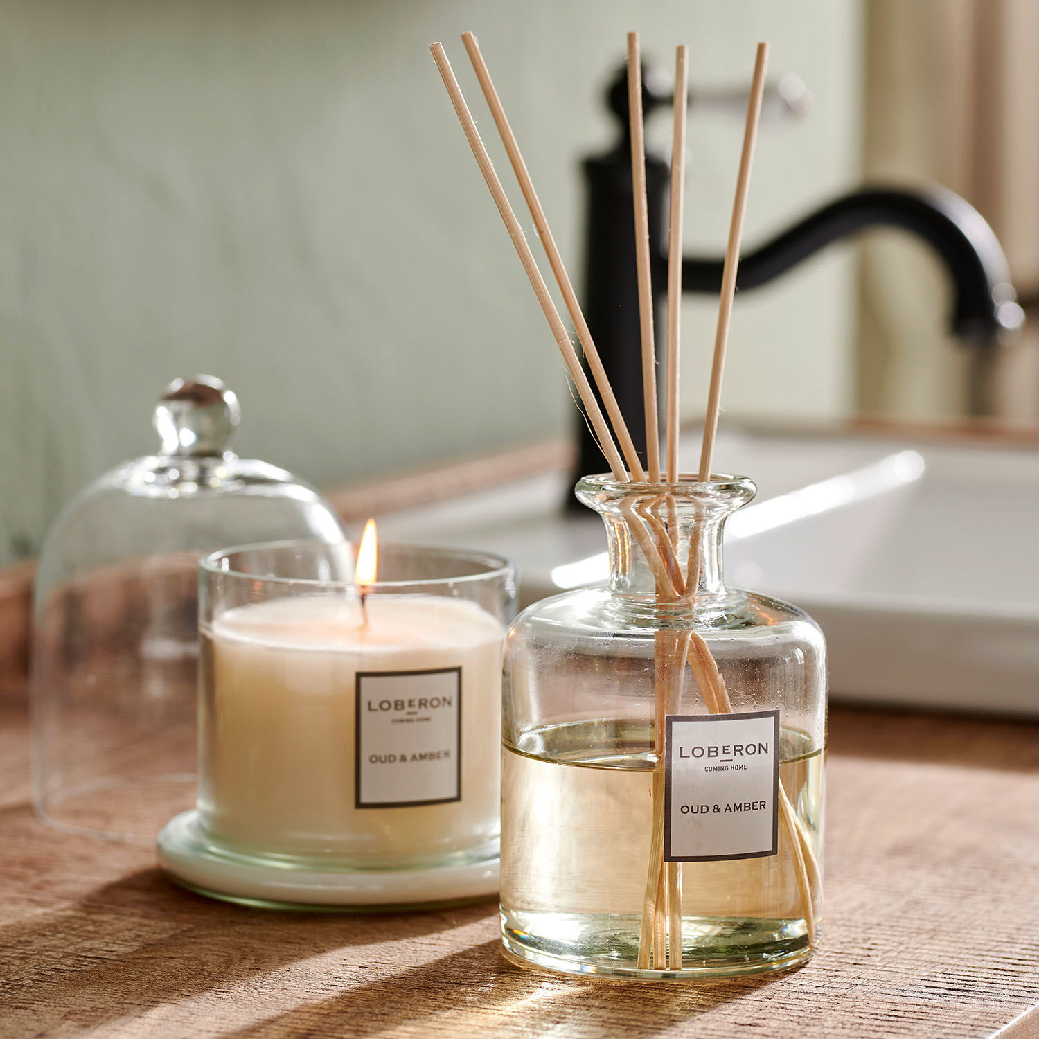 Set di profumatori per ambienti Vanis Candela e diffusore profumato Oud & Amber in vetro su piano in legno in bagno