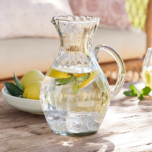 Caraffa di vetro con acqua, ghiaccio e fette di limone su tavolo in legno, bevanda estiva