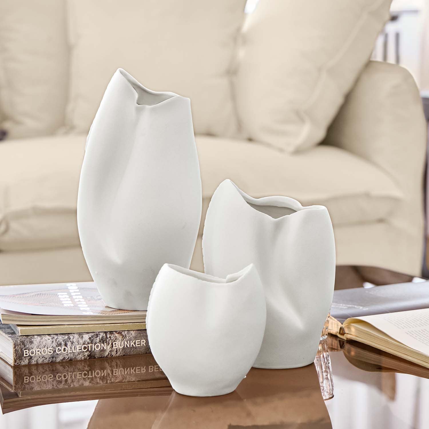 Set di tre vasi in ceramica bianca con forme irregolari su un tavolo con libri
