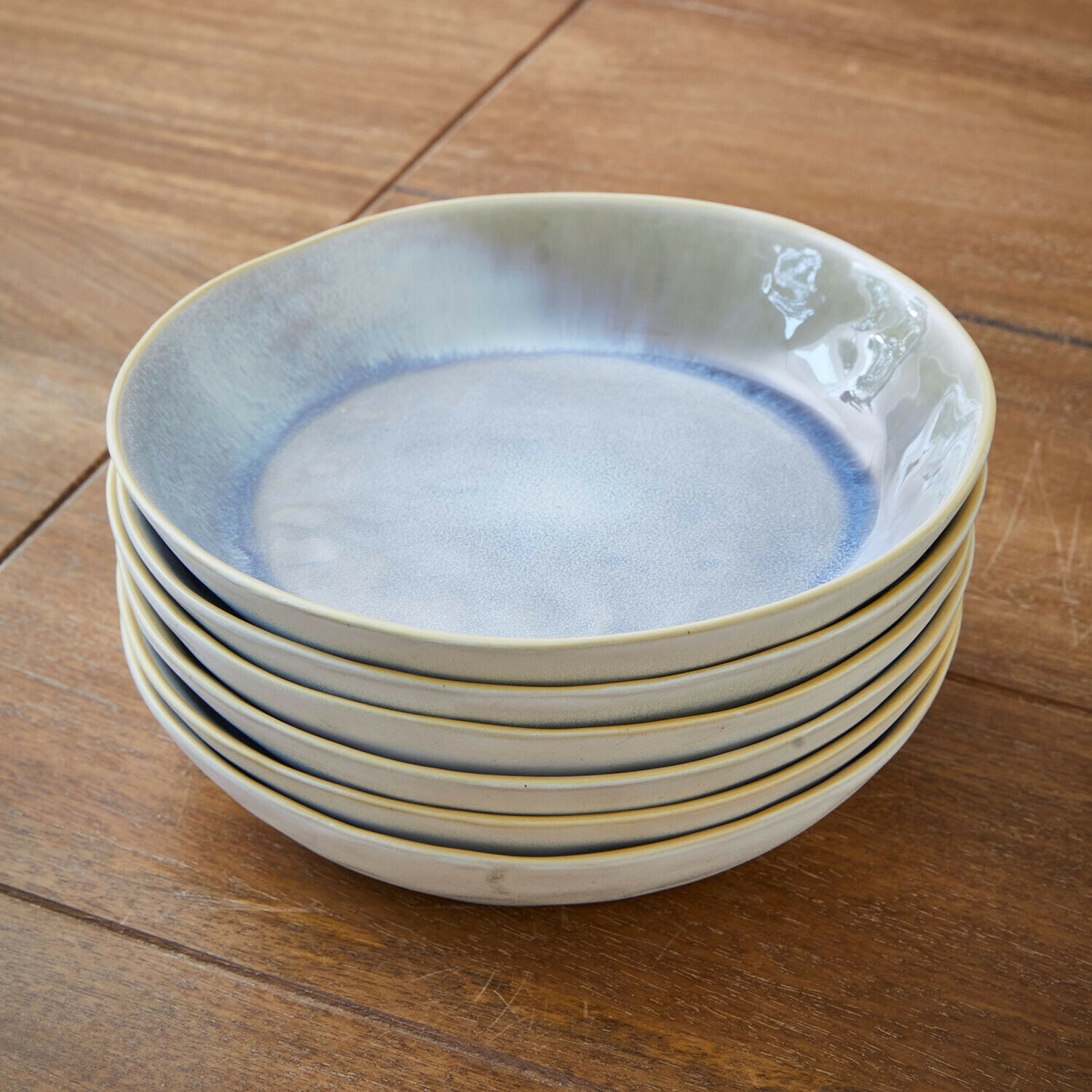Set di sei piatti in ceramica blu e beige impilati su tavolo in legno