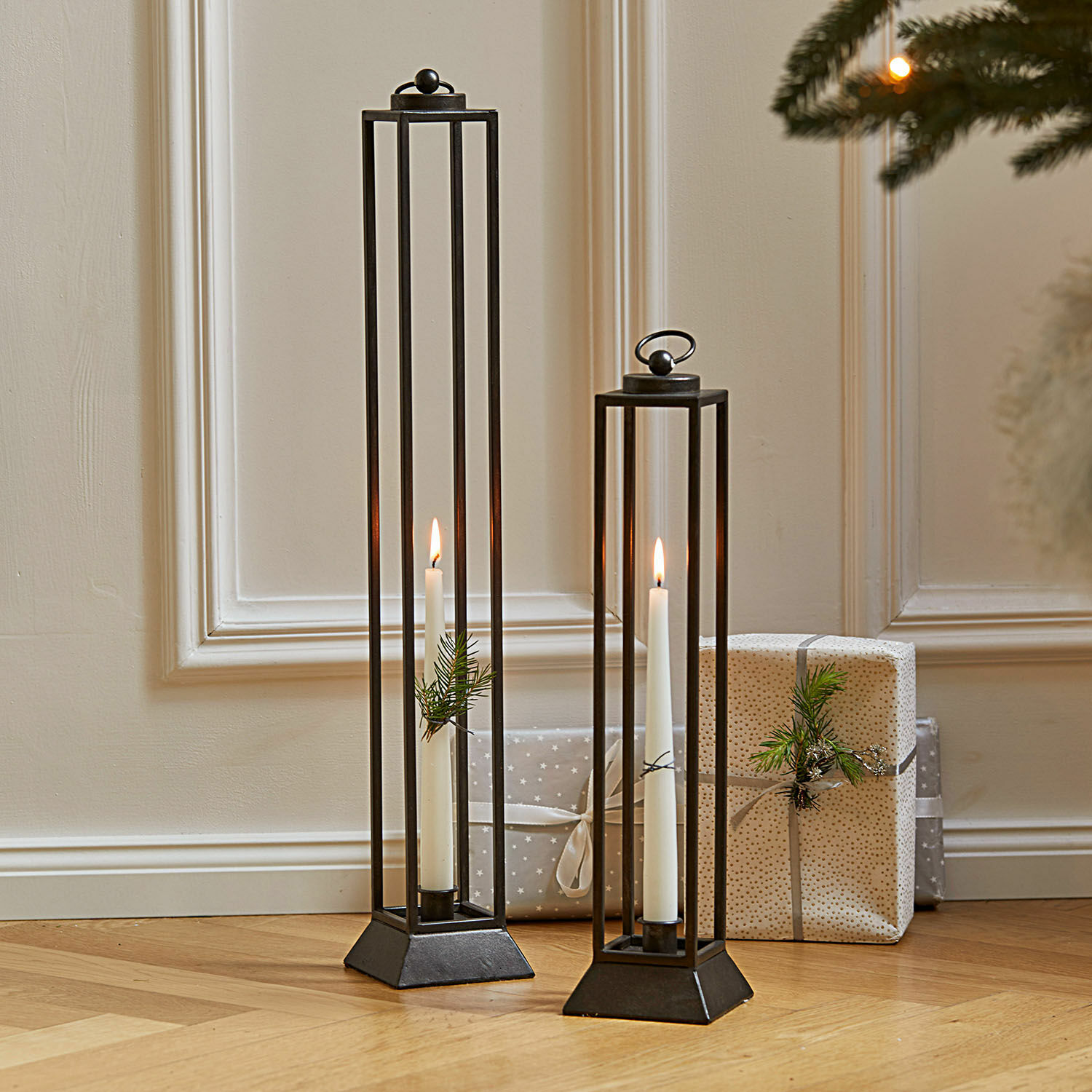 Coppia di lanterne Régat Due lanterne in metallo nero con candele bianche e decorazioni di rami su pavimento in legno