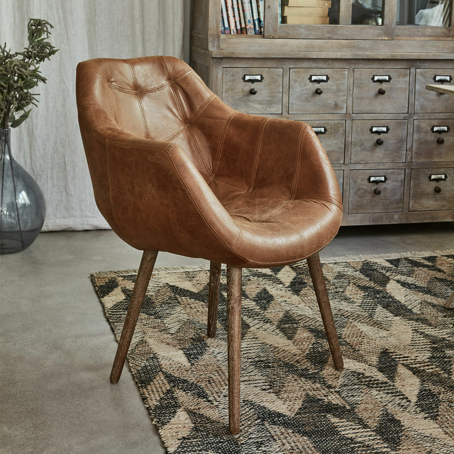 Sedia Montigny Poltrona marrone in ecopelle con gambe in legno su tappeto geometrico in soggiorno