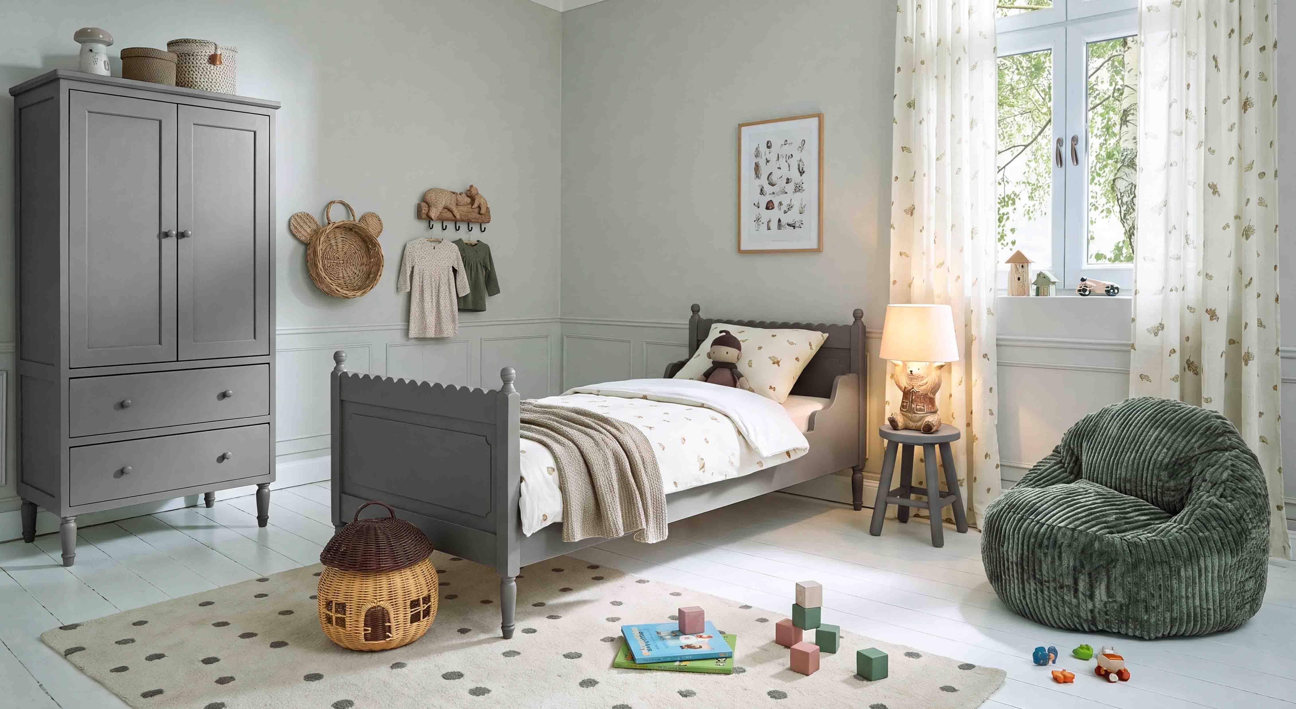 Armadio e letto in legno grigio in camera bambini con poltrona verde morbida e decorazioni