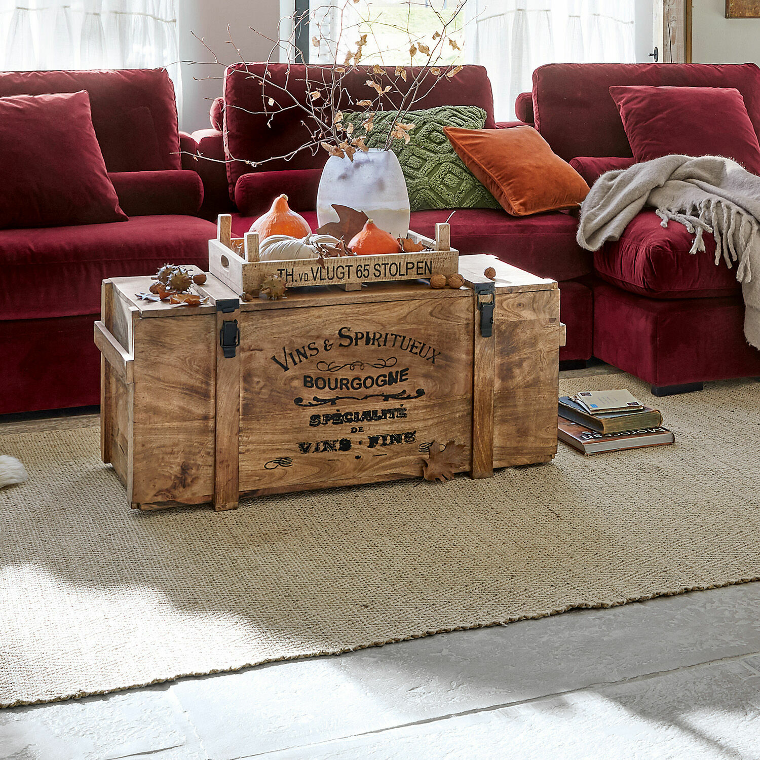 Baule Eskeny Cassa in legno con scritta su tappeto davanti a divano bordeaux con cuscini e coperta in soggiorno