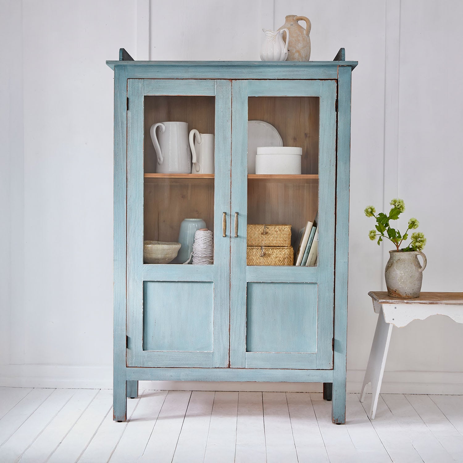 Mobile in legno blu con ante in vetro e decorazioni in ceramica vintage in ambiente luminoso
