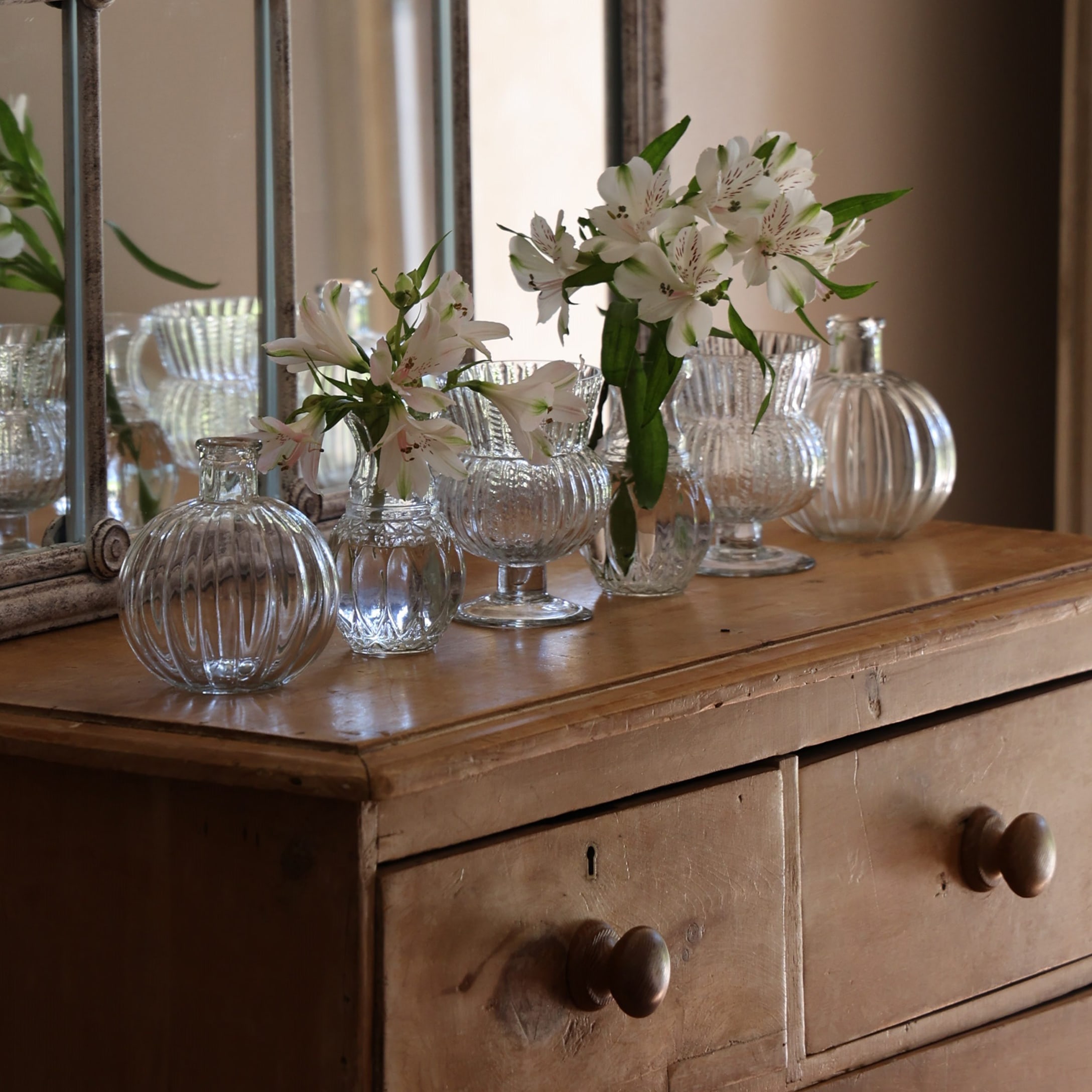 Set di vasi in vetro trasparente con fiori bianchi su comò in legno vintage