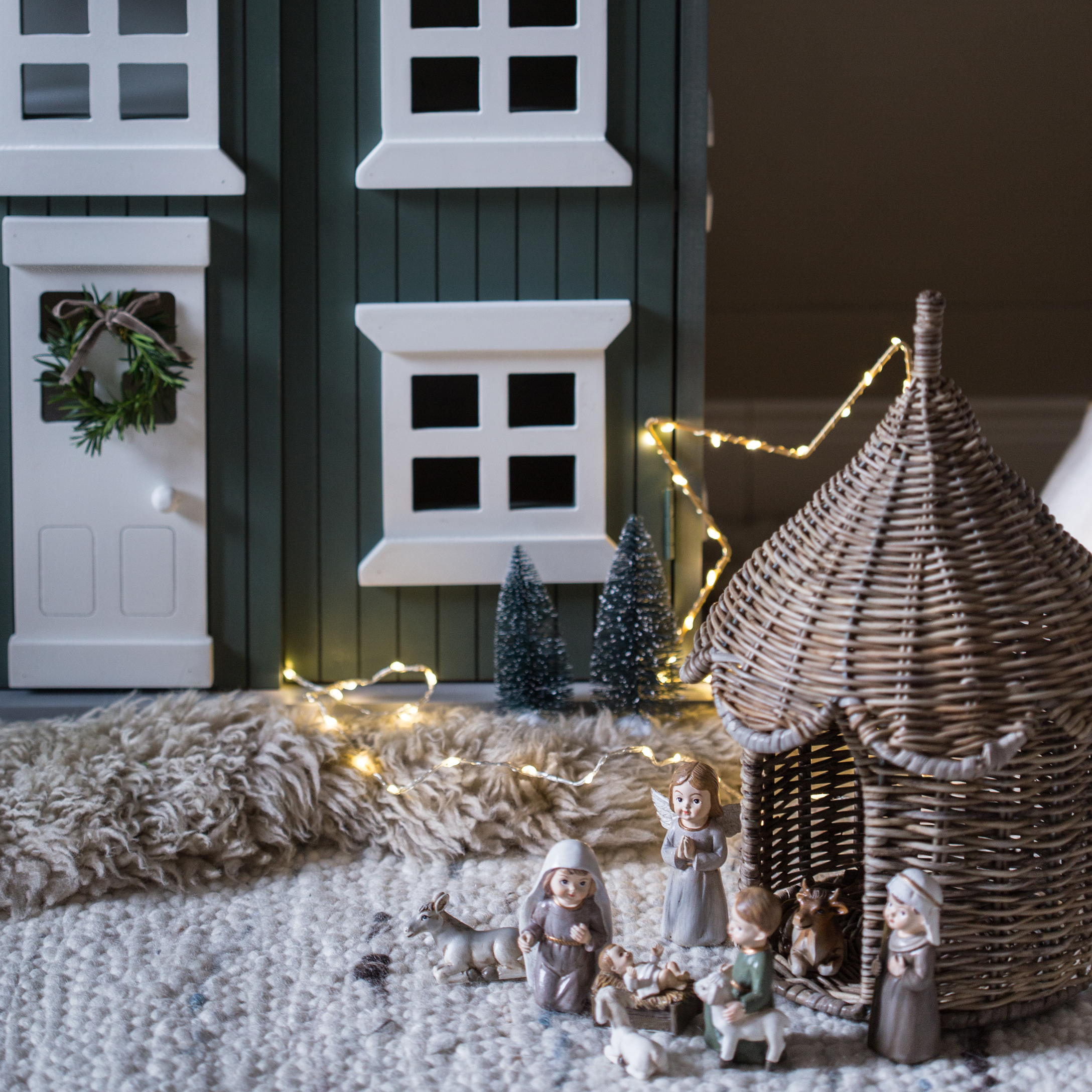 Decorazione natalizia con statuine del presepe e capanna in vimini su tappeto con luci LED