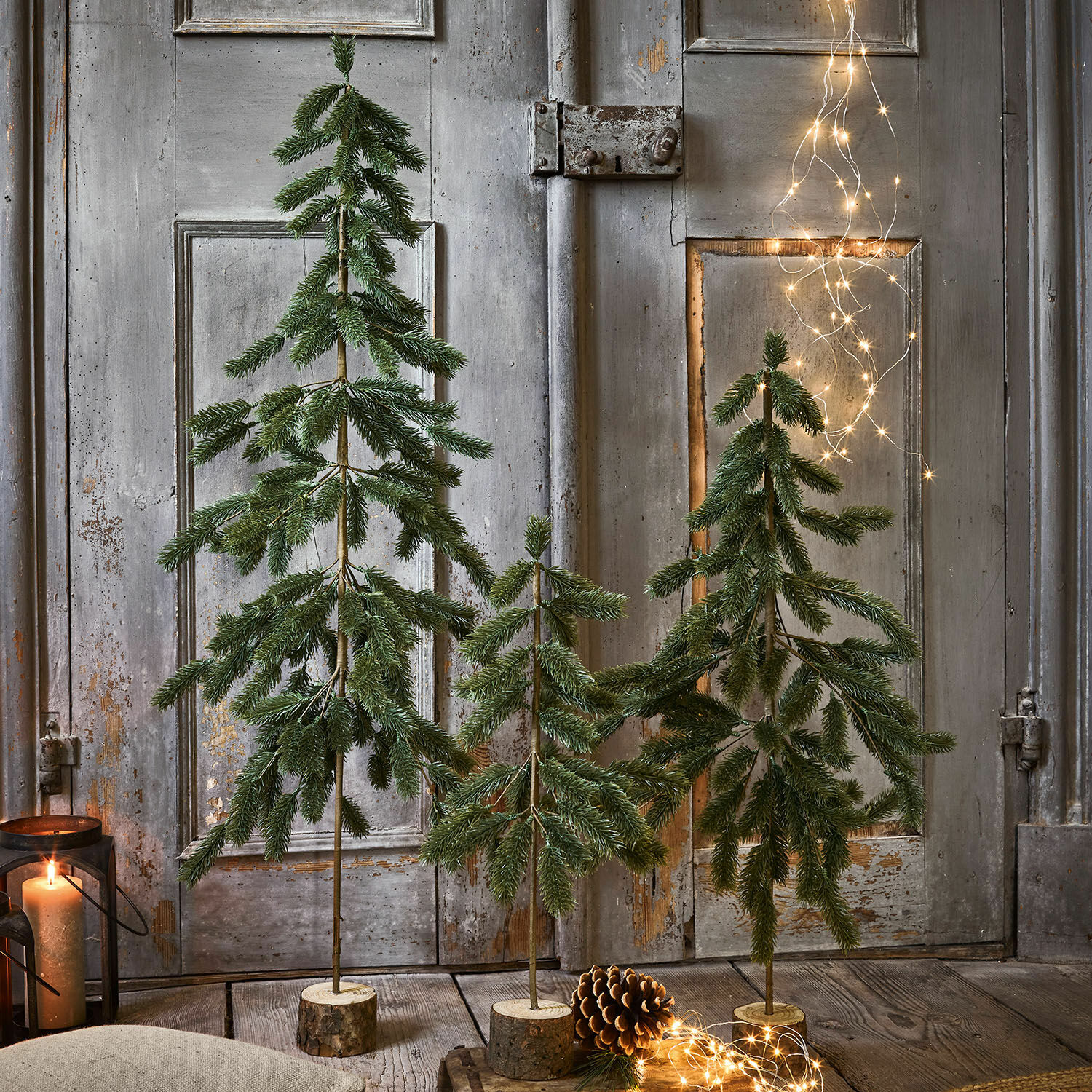 Set di 3 alberelli di Natale Lorin Tre alberi decorativi verdi con base in legno, luci LED e pigna decorativa in primo piano