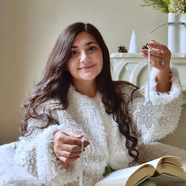 Donna con maglione bianco soffice che tiene decorazione natalizia bianca a forma di fiocco di neve con libro aperto sulle ginocchia