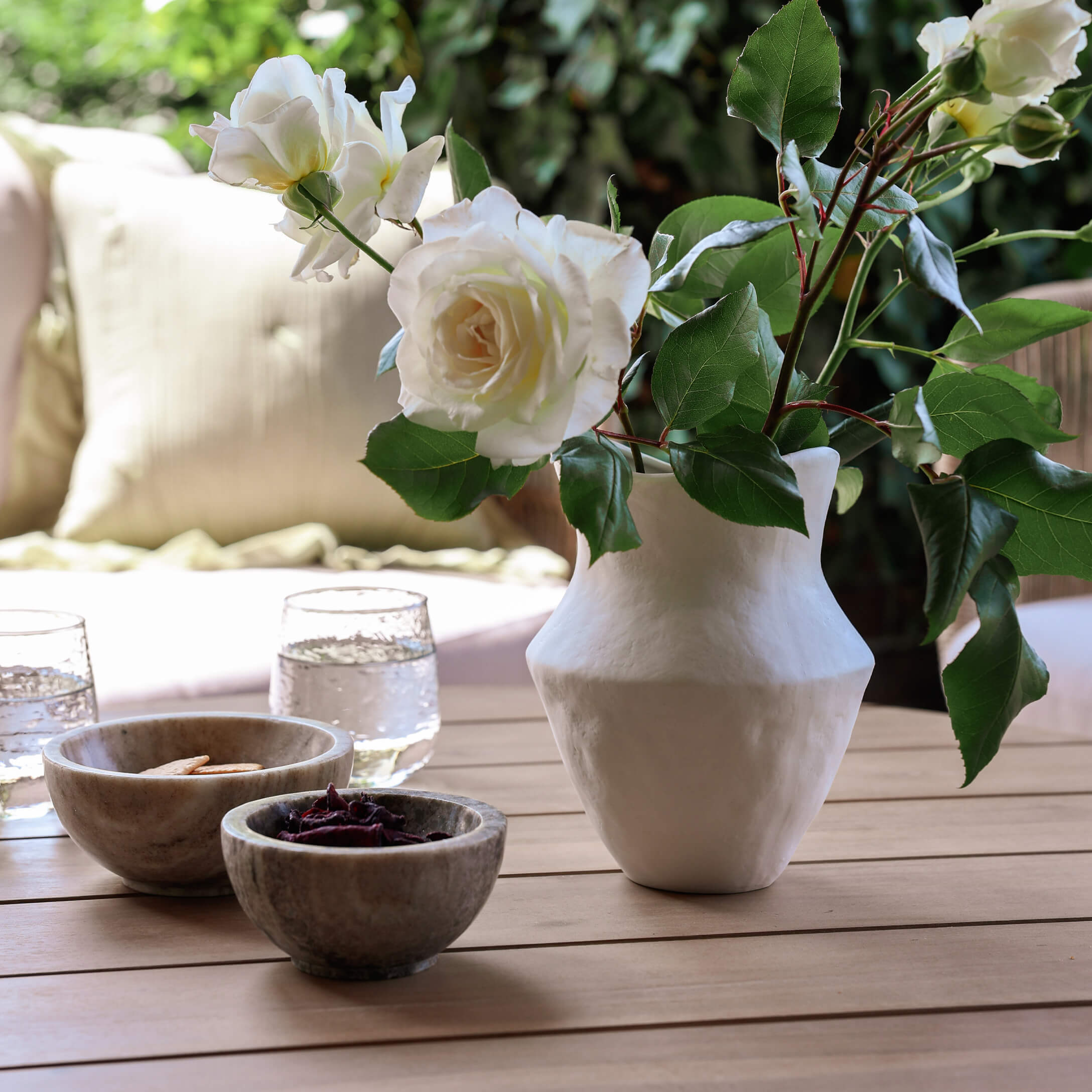 Vaso in ceramica bianca con rose bianche su tavolo in legno con ciotole e bicchieri d'acqua