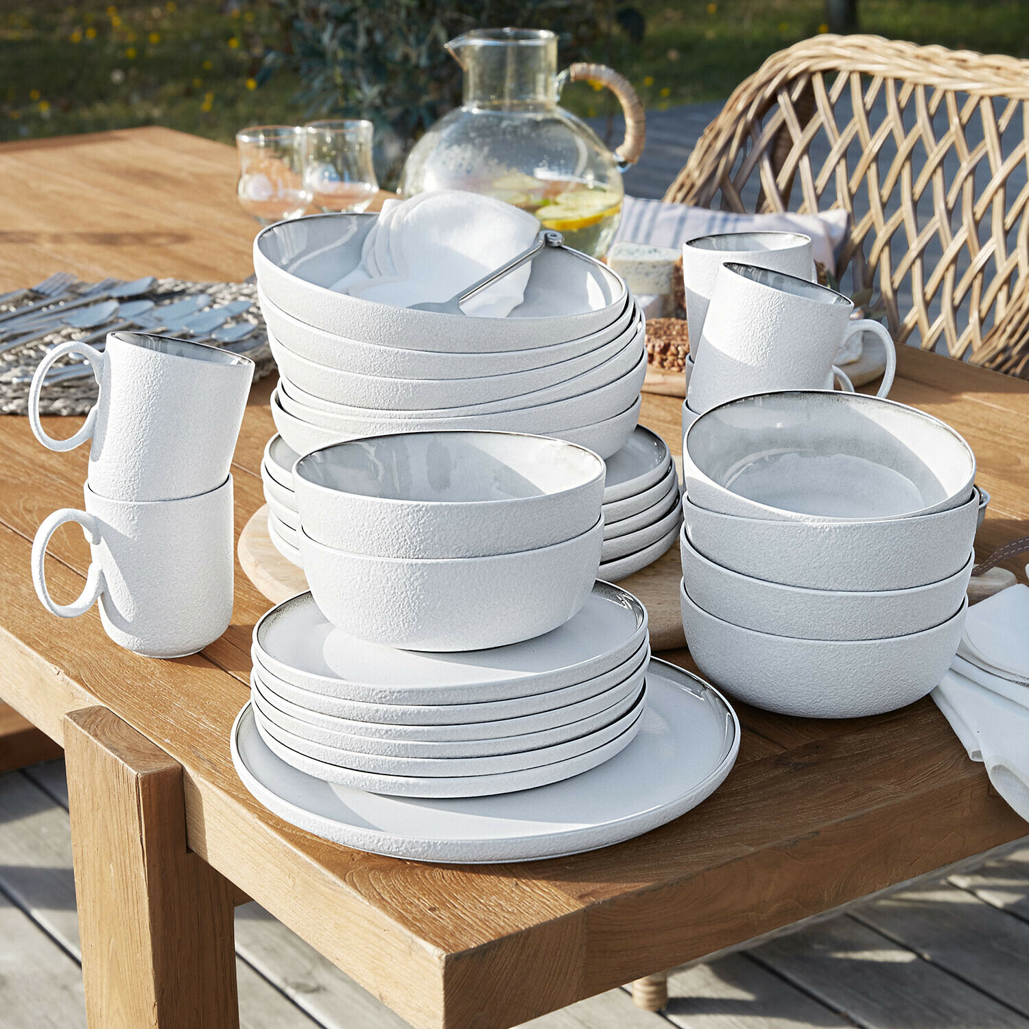 Set di 30 stoviglie Eiruna Set di stoviglie in ceramica bianca con superficie strutturata impilate su tavolo in legno all'aperto