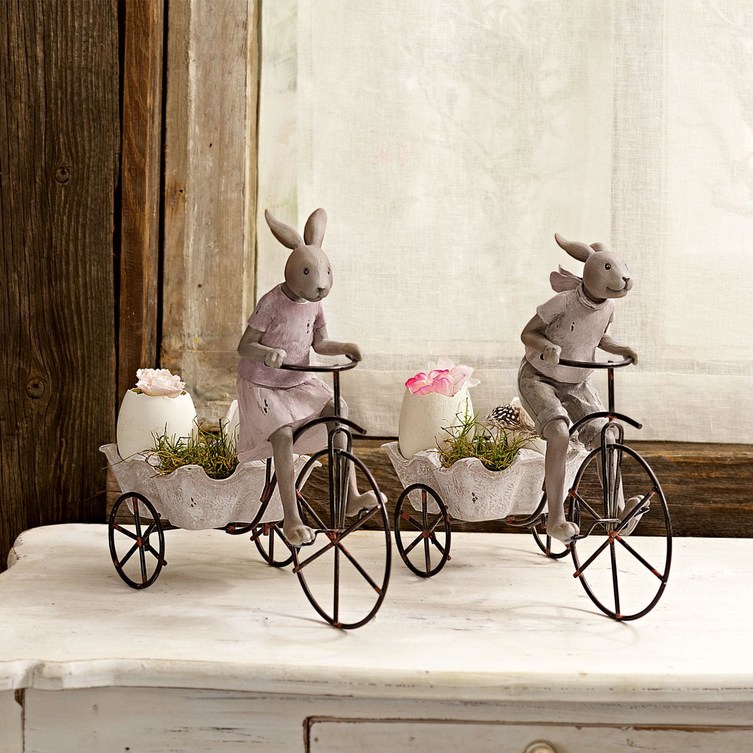 Figure decorative di conigli su biciclette in metallo con vasi bianchi e fiori su tavolo