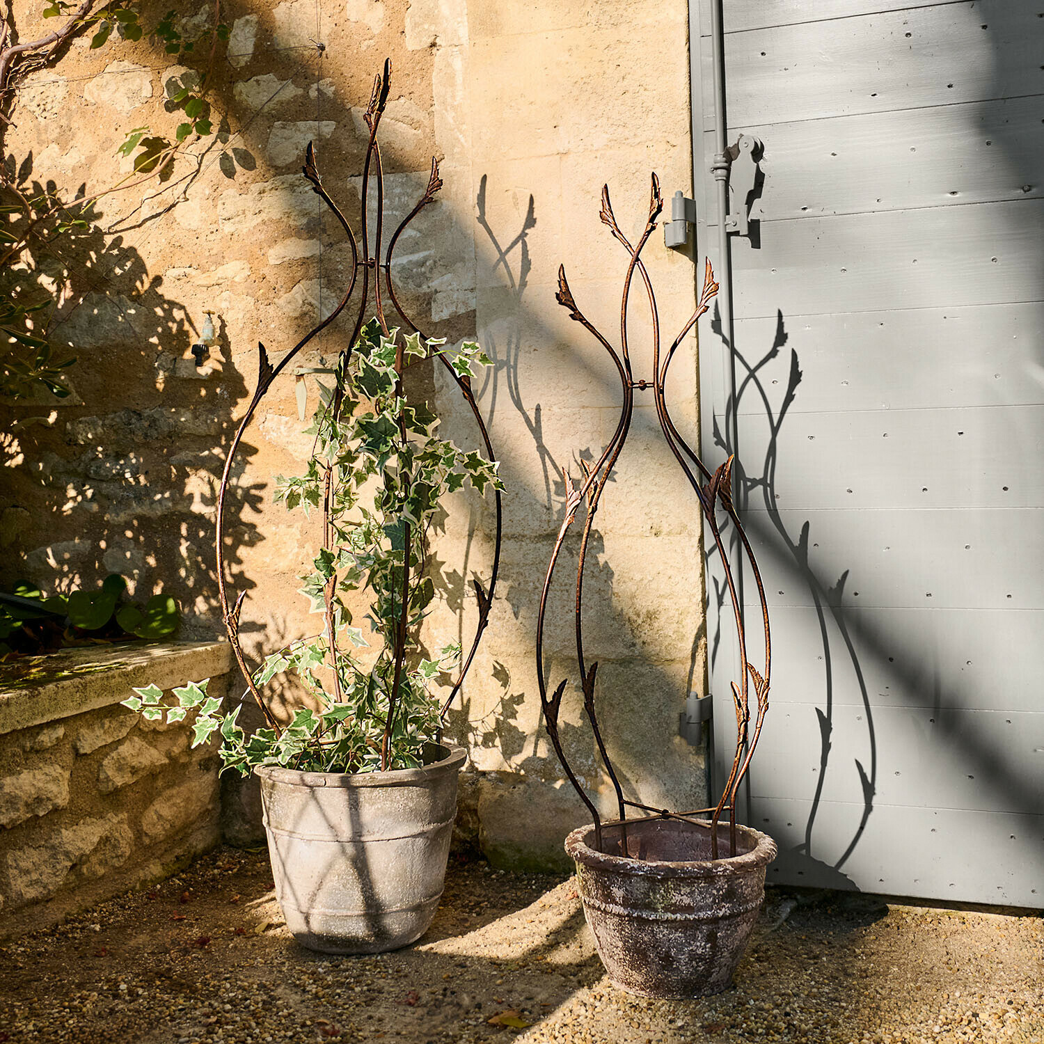 Due supporti decorativi in metallo per piante in vasi di pietra su terrazza soleggiata