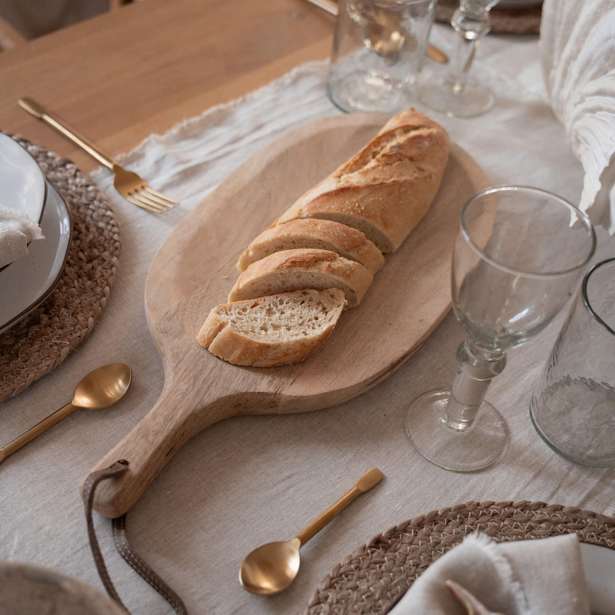 Tagliere in legno con baguette affettata su tavola con stoviglie e posate dorate