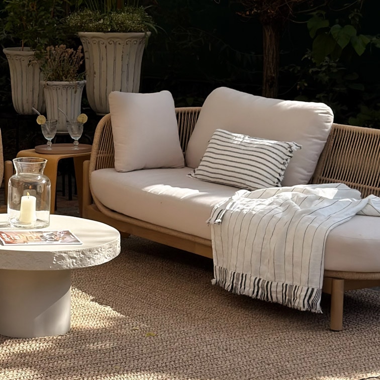 Divano da esterno moderno con cuscini chiari e plaid a righe su tappeto naturale in giardino