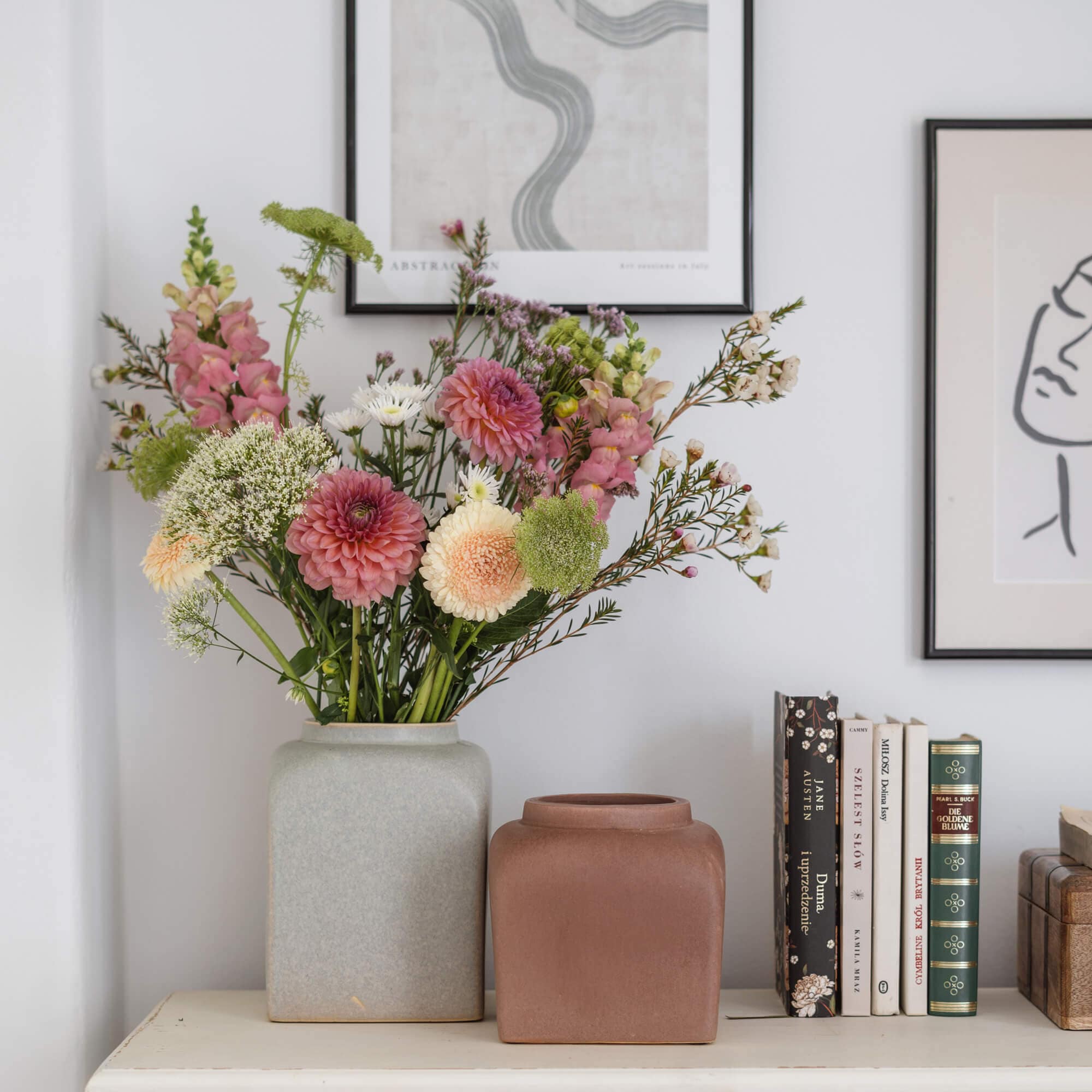 Due vasi in ceramica grigio e marrone su tavolo bianco con mazzo di fiori e libri