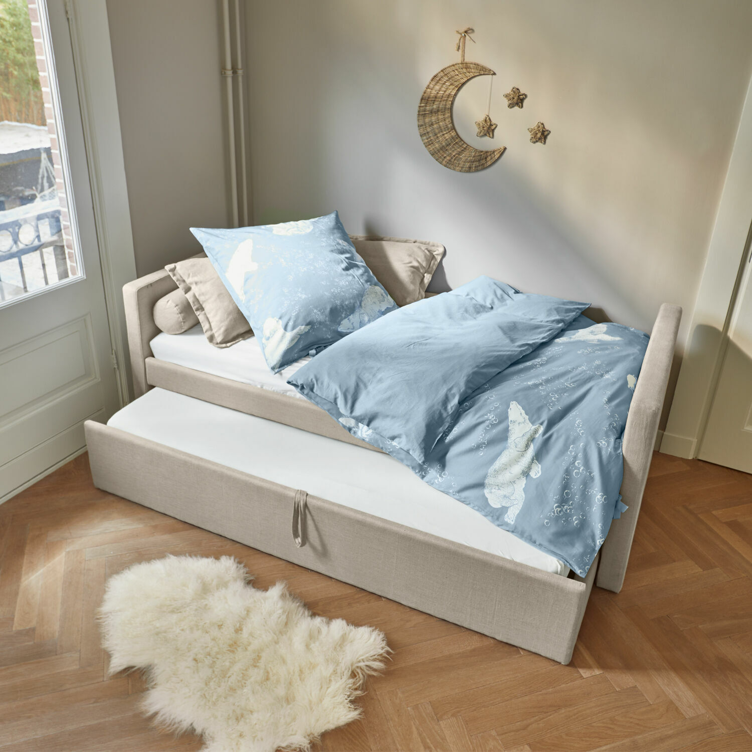 Letto Thistlewood Letto beige con materasso estraibile e biancheria da letto azzurra con motivo orso polare in stanza luminosa.