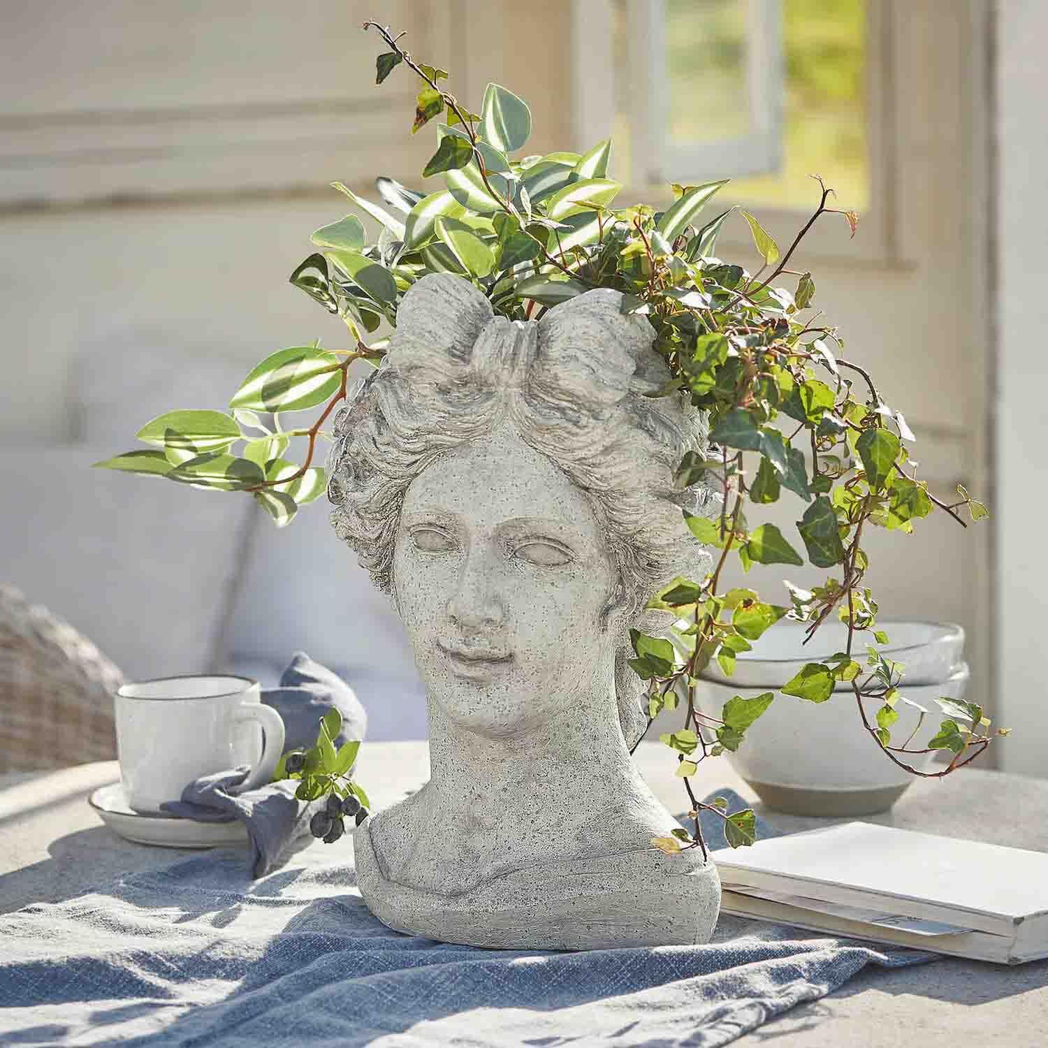Vaso a forma di testa di donna in pietra grigia con piante verdi, decorazione da giardino