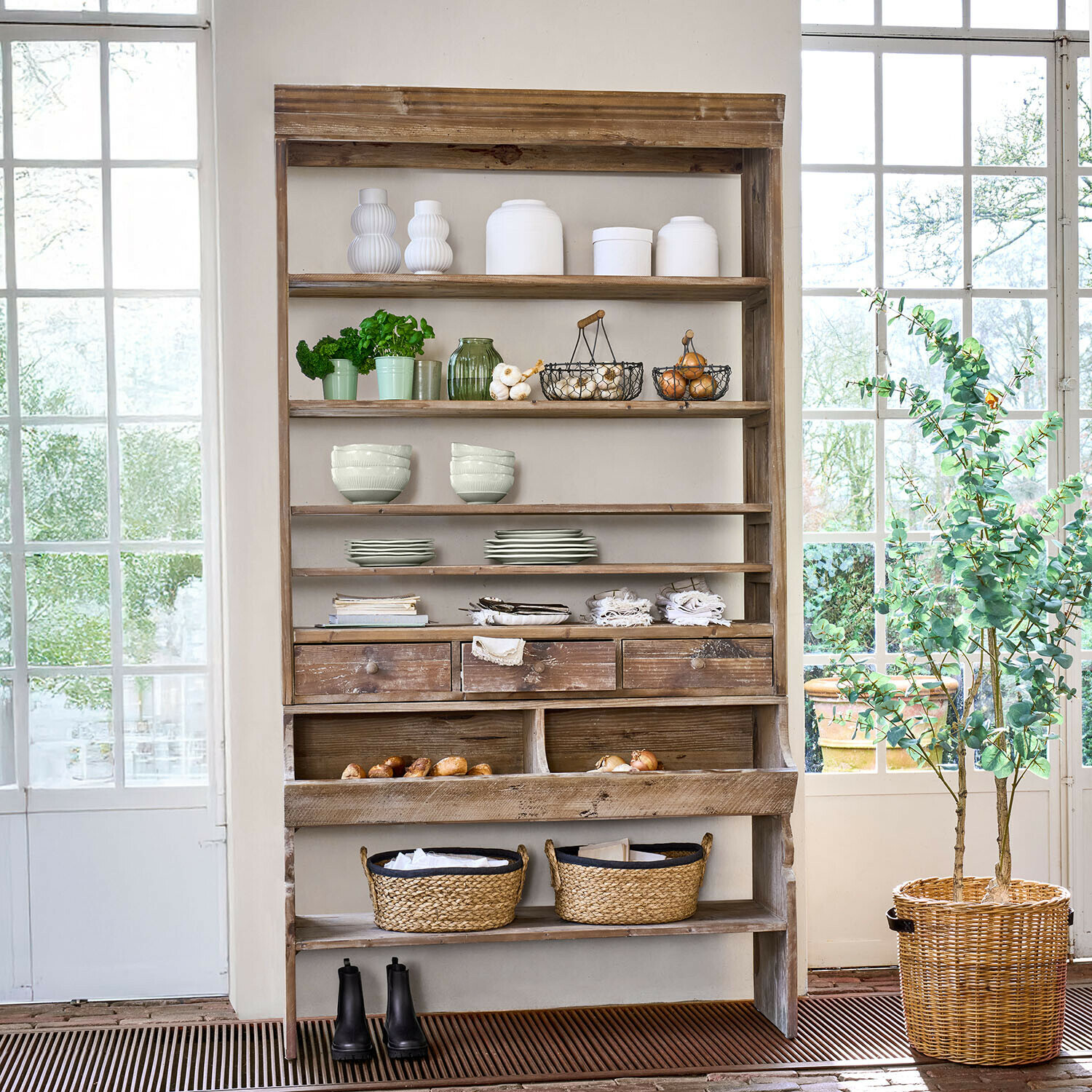 Scaffale rustico in legno con ceramica bianca, vasi verdi e cesti di vimini per riporre oggetti