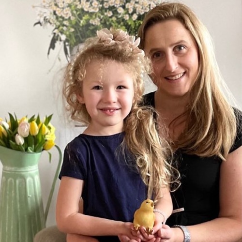 Donna sorridente e bambina bionda tengono decorazione a forma di uccello giallo in interno luminoso