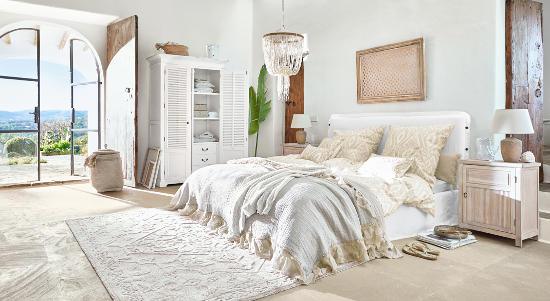 Camera luminosa con letto bianco, biancheria da letto beige e mobili rustici in legno