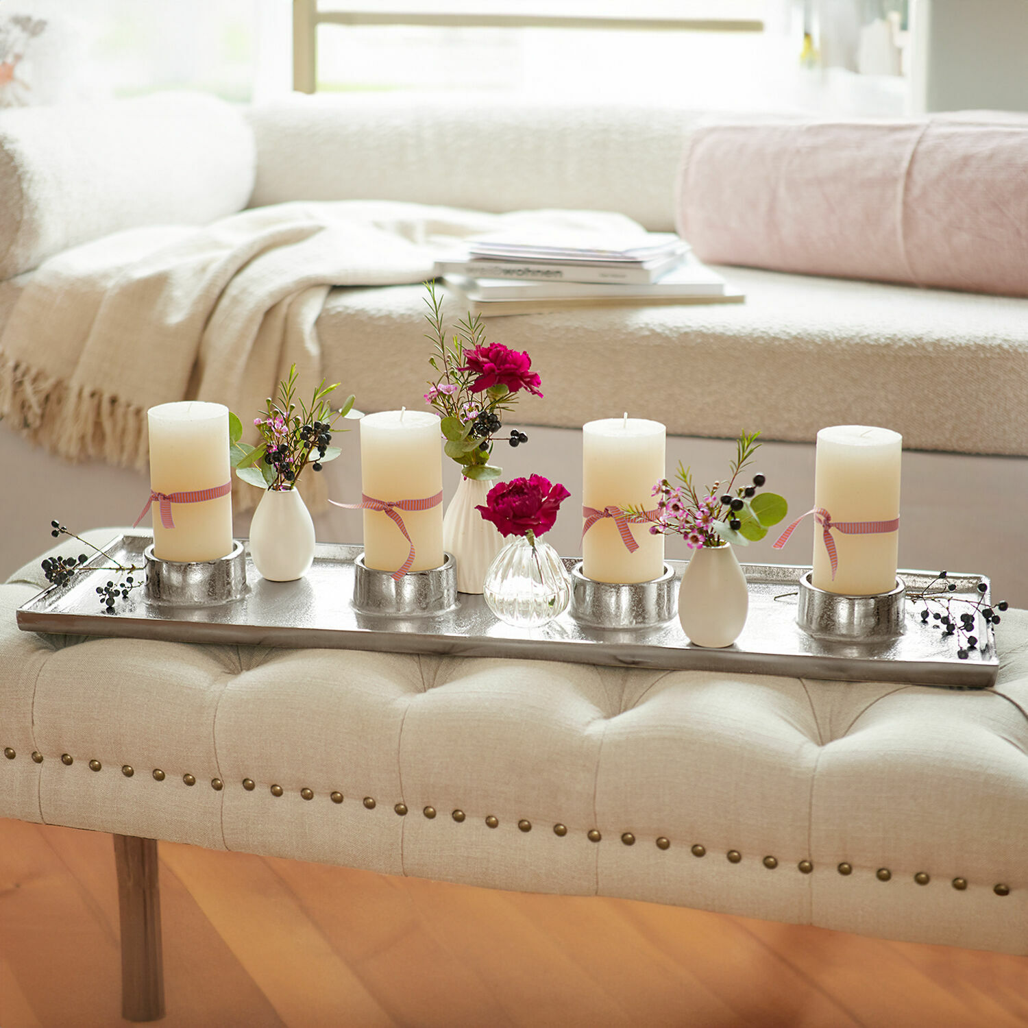 Portacandele Mareuil Vassoio in metallo con quattro candele crema e piccoli vasi con fiori su panca beige