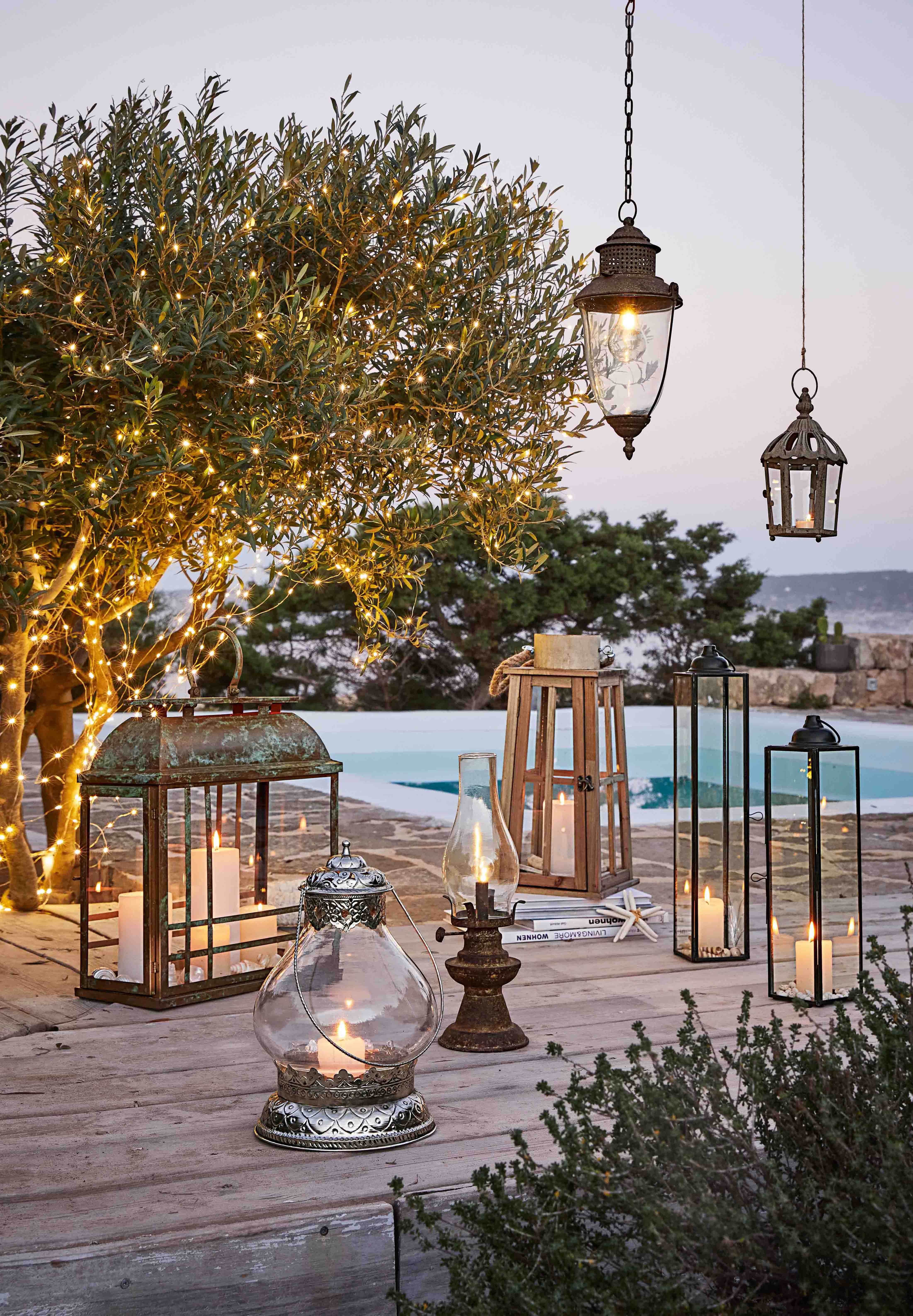 Set di lanterne e candele su terrazza in legno con albero decorato con luci LED