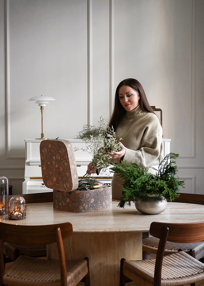 Donna con maglione beige sistema fiori su tavolo in marmo con scatola decorativa e piante verdi
