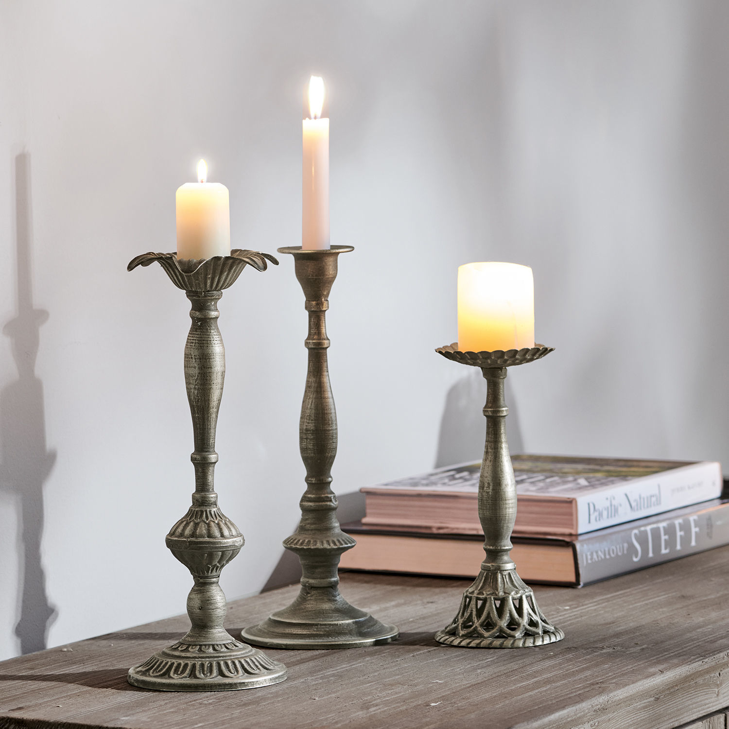 Set di 3 candelieri Chandra Tre portacandele in metallo color argento antico con candele accese su tavolo in legno