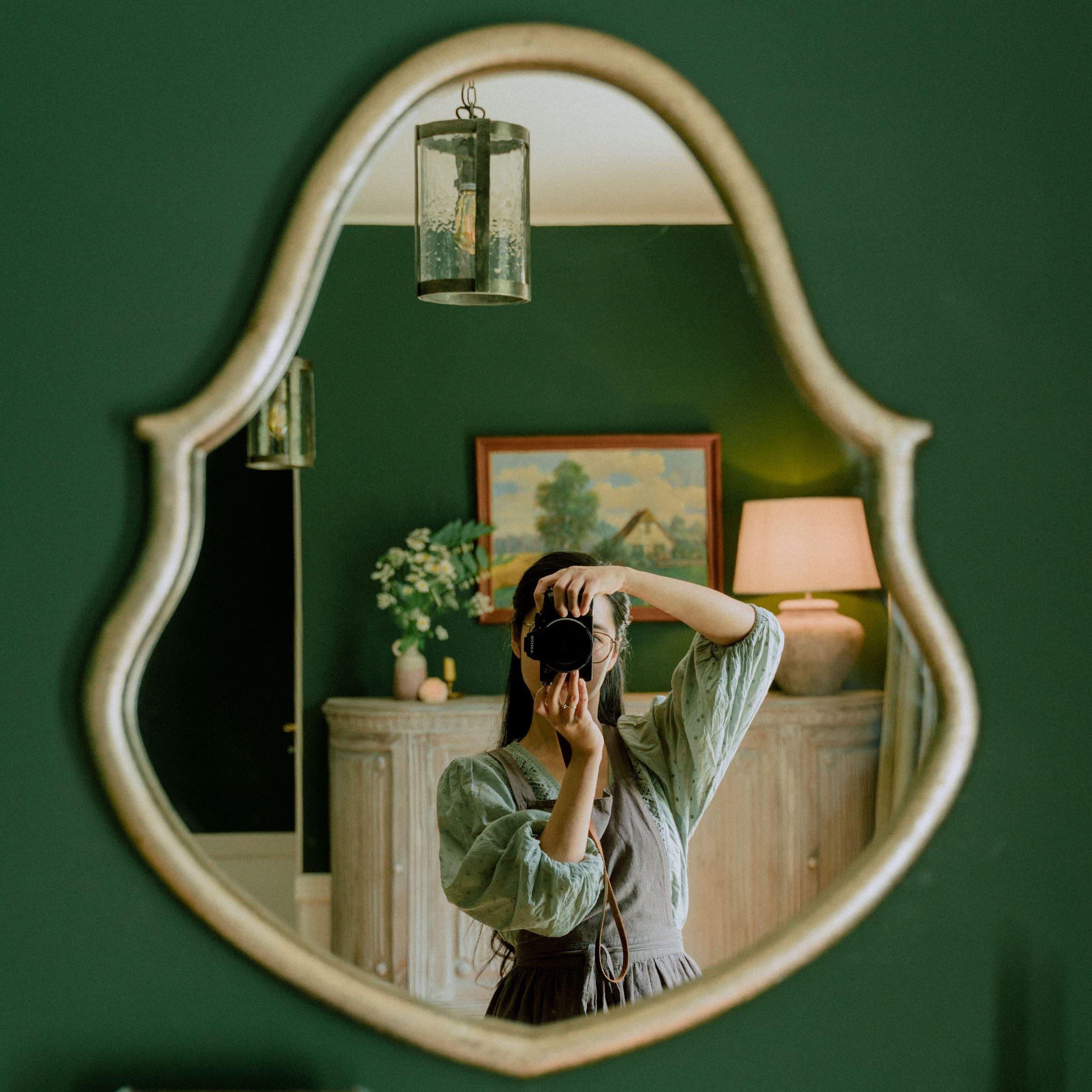 Specchio ovale con cornice decorativa su parete verde in interno elegante con lampada e quadro