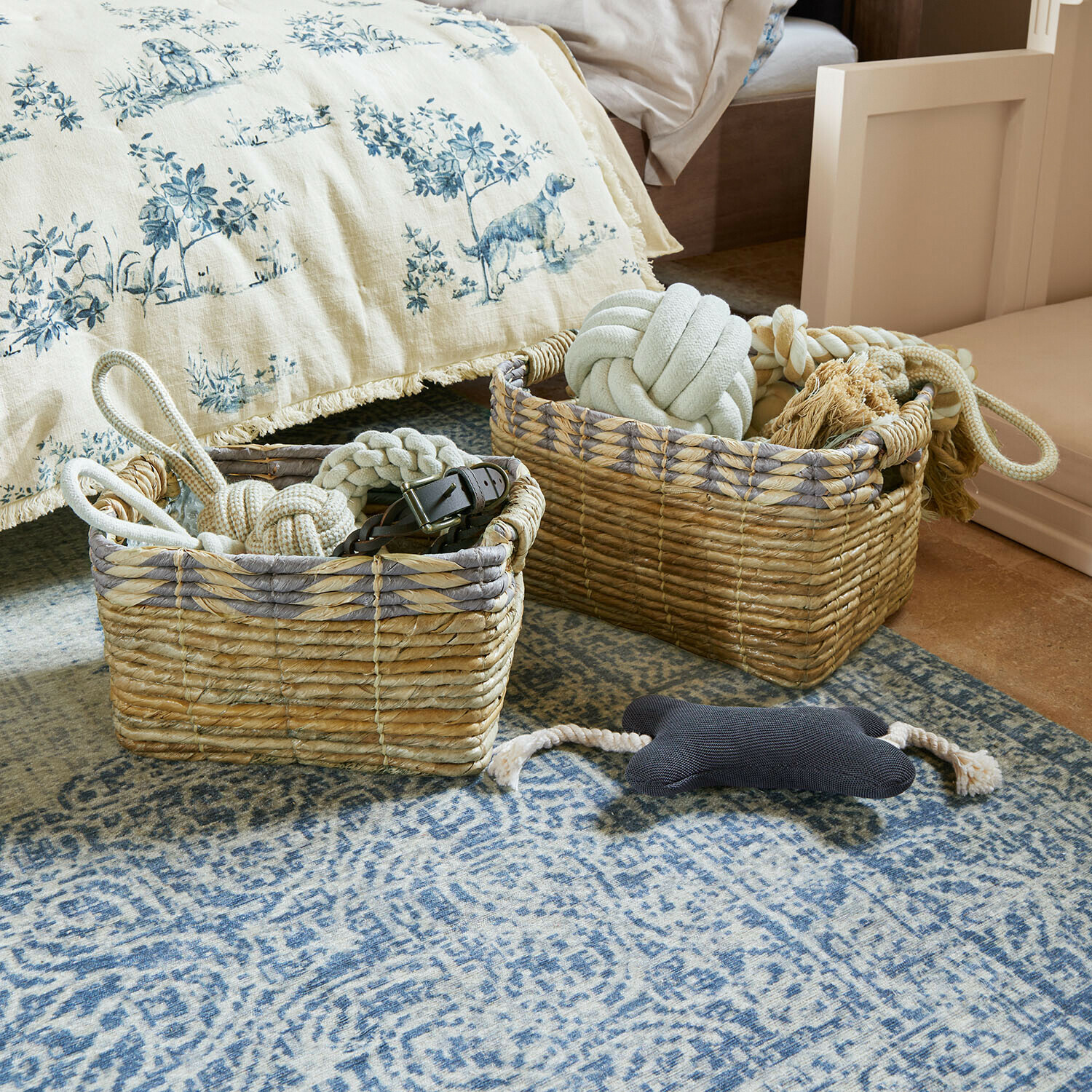 Due ceste in vimini naturale con giocattoli per cani su tappeto blu in camera da letto