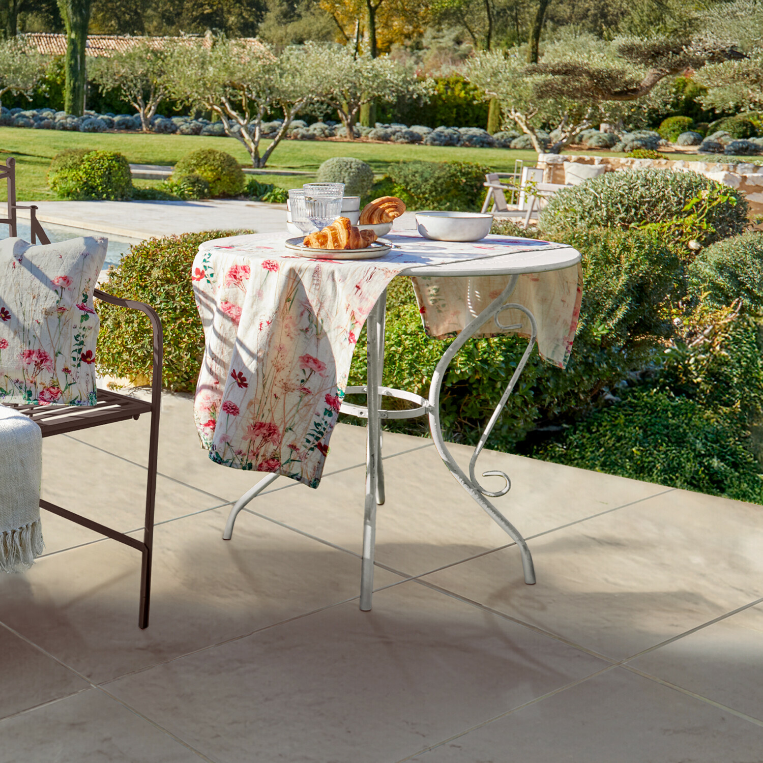 Tavolino Aube Tavolo da giardino rotondo in metallo bianco con tovaglia floreale e pasticceria su terrazza con vista giardino
