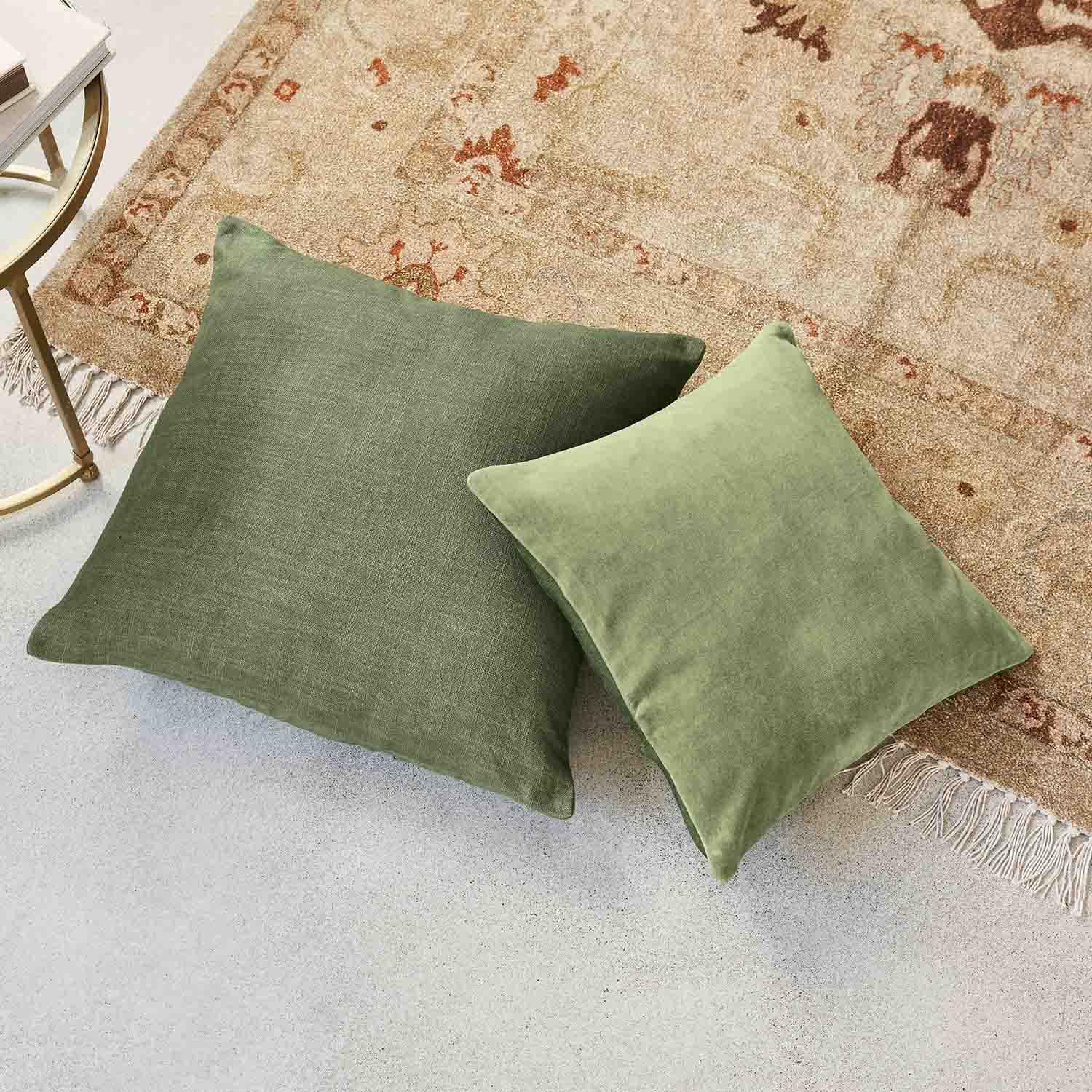 Due cuscini verdi in tessuto su tappeto beige con frange, accessori decorativi per un soggiorno accogliente