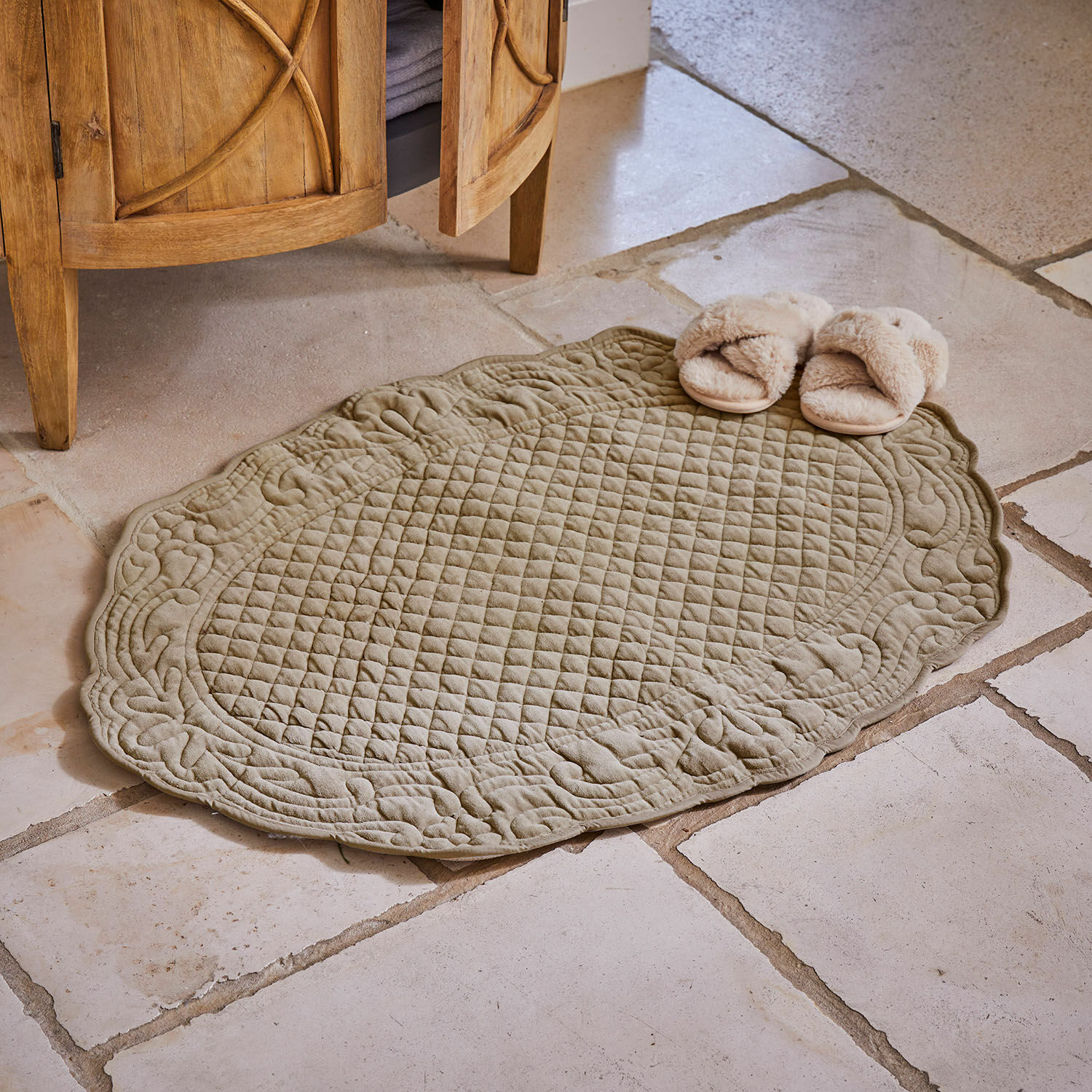 Scendibagno Courlevin Tappeto ovale trapuntato in cotone verde oliva su pavimento in pietra con pantofole beige