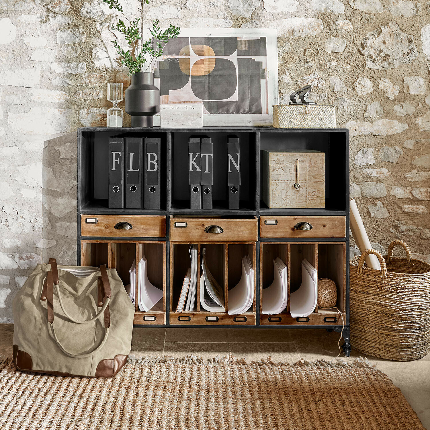 Credenza bassa Fenwicke Mobile nero in metallo e legno con cassetti e raccoglitori davanti a muro in pietra stile vintage