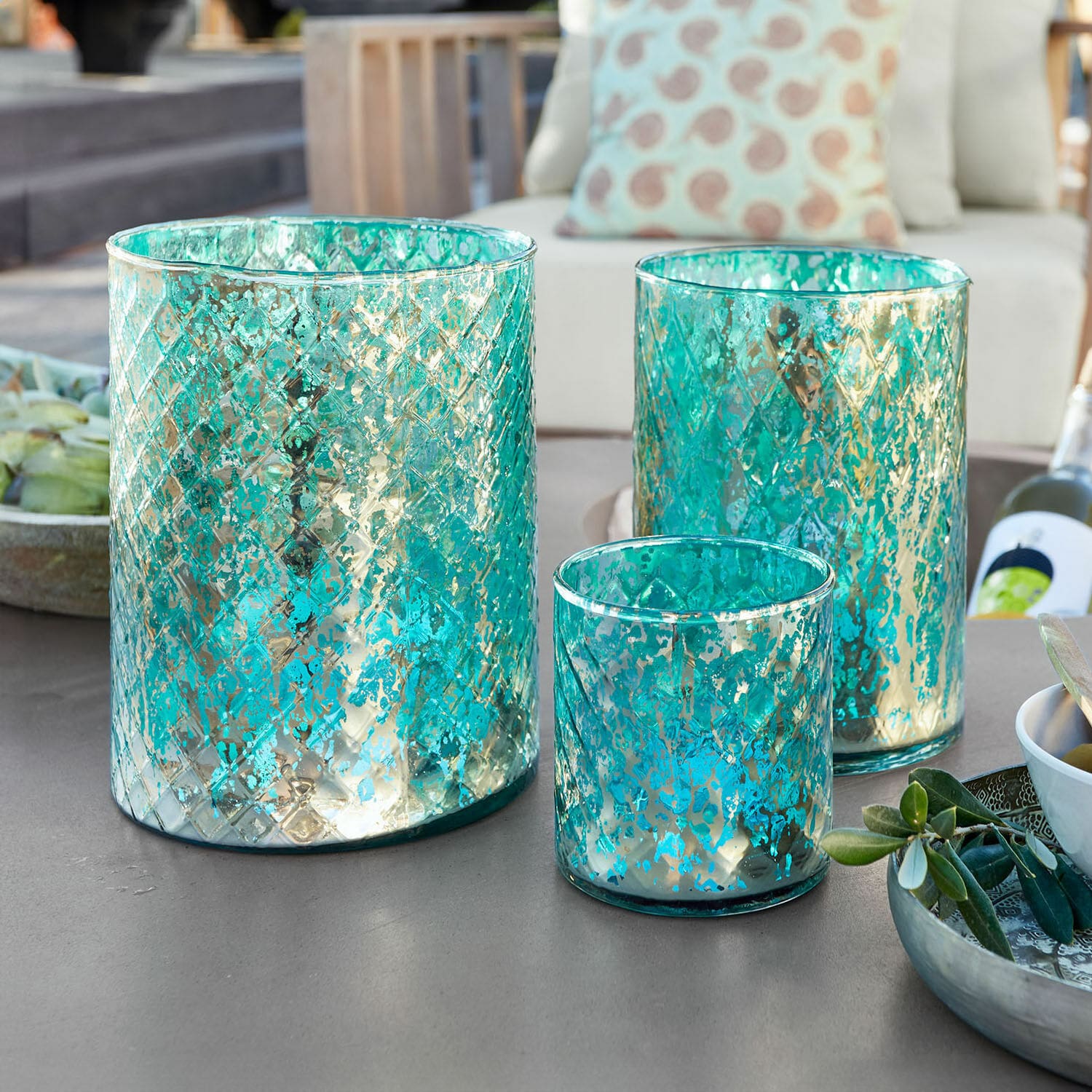 Set di 3 lanterne Firalen Set di tre portacandele in vetro turchese con motivo metallico su tavolo da giardino