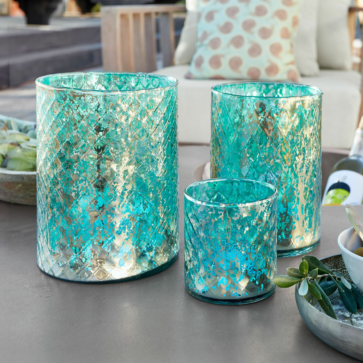 Set di 3 lanterne Firalen Set di tre portacandele in vetro turchese con motivo metallico su tavolo da giardino
