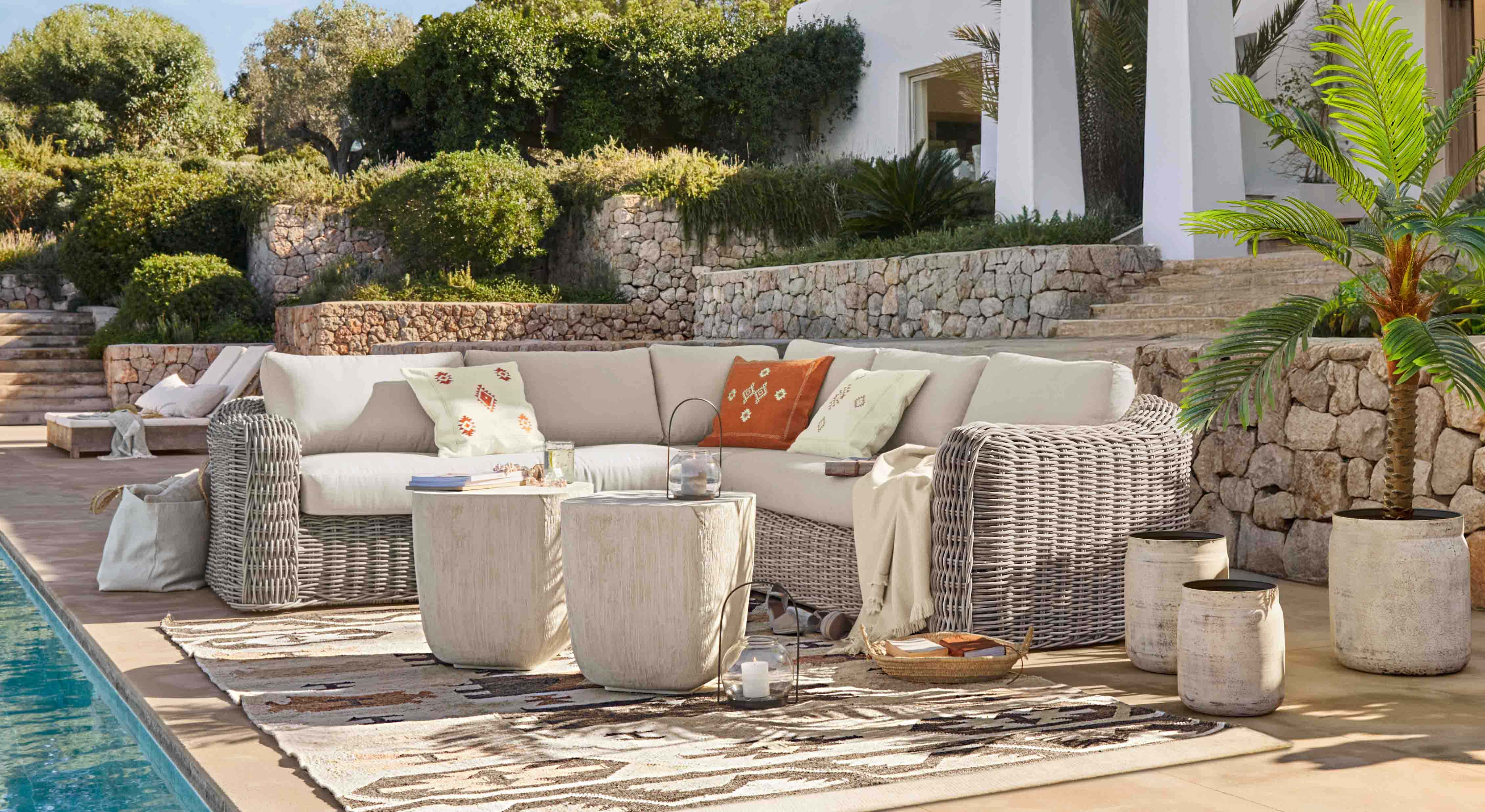 Set di mobili da giardino in rattan grigio chiaro con cuscini crema e cuscini decorativi su terrazza vicino alla piscina