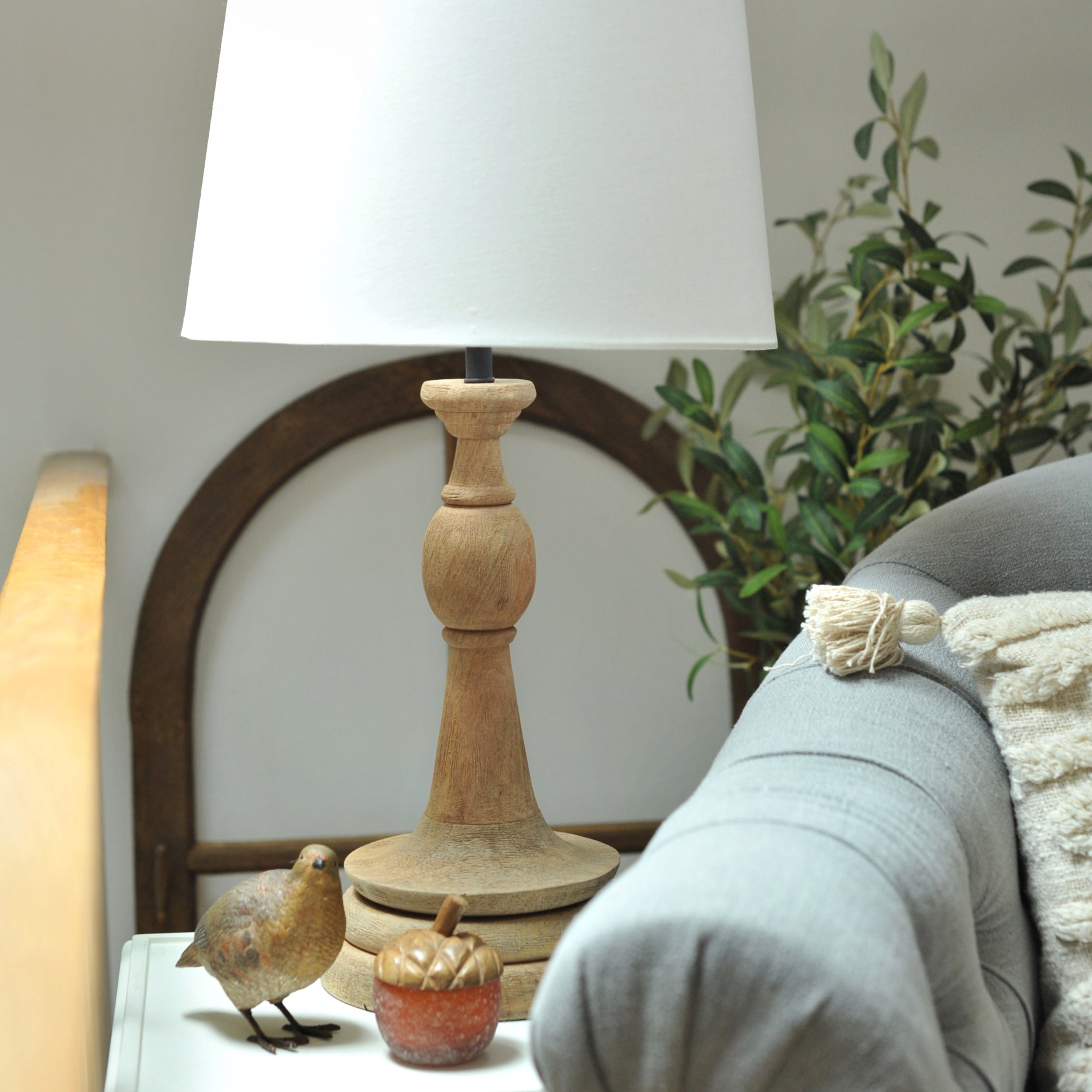 Lampada da tavolo con base in legno e paralume bianco su tavolino accanto a divano grigio e decorazioni