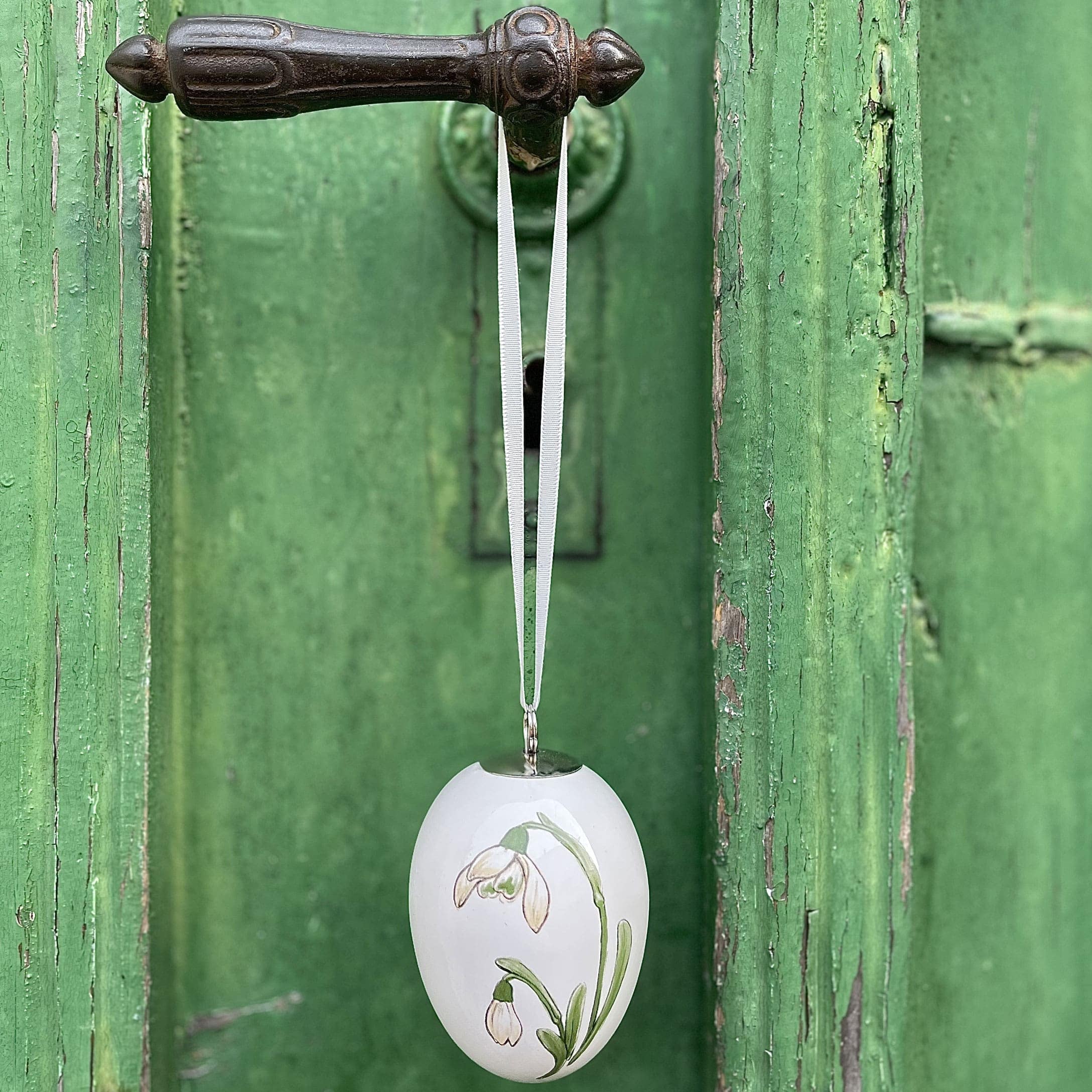 Decorazione pasquale a forma di uovo in ceramica bianca con motivo floreale appesa a porta verde